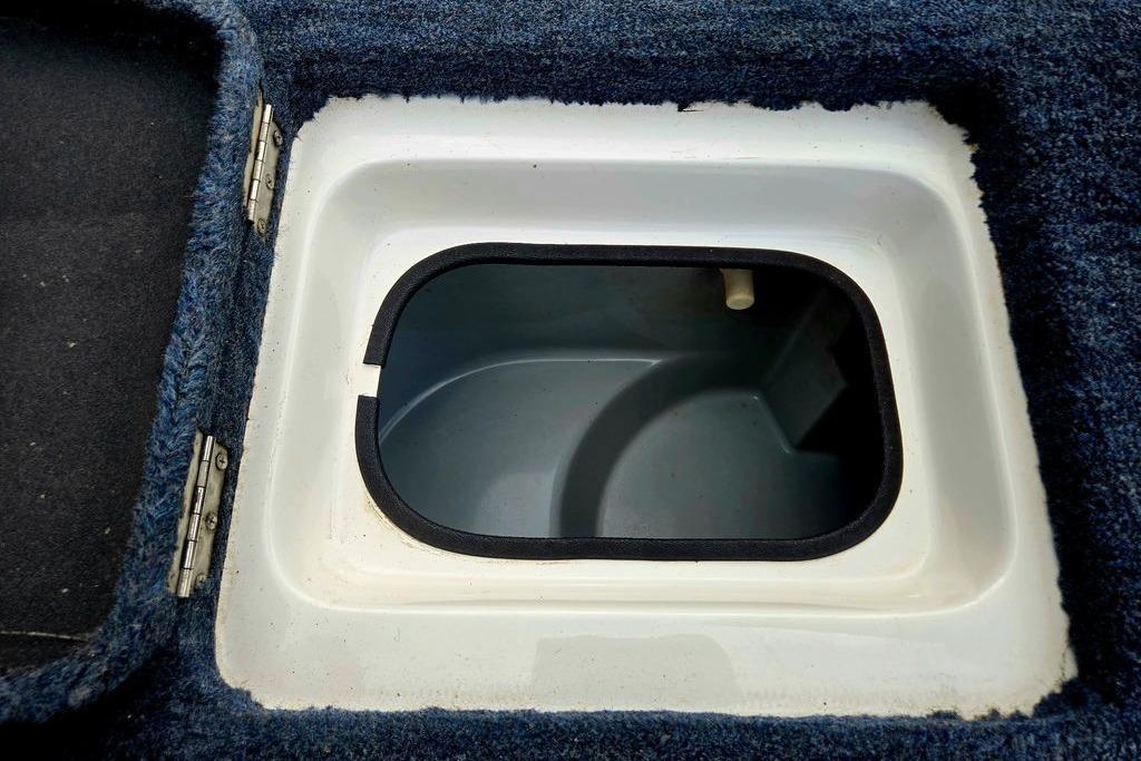 Open storage compartment in 1996 Champion 181 SX boat, featuring blue carpeted edges.
