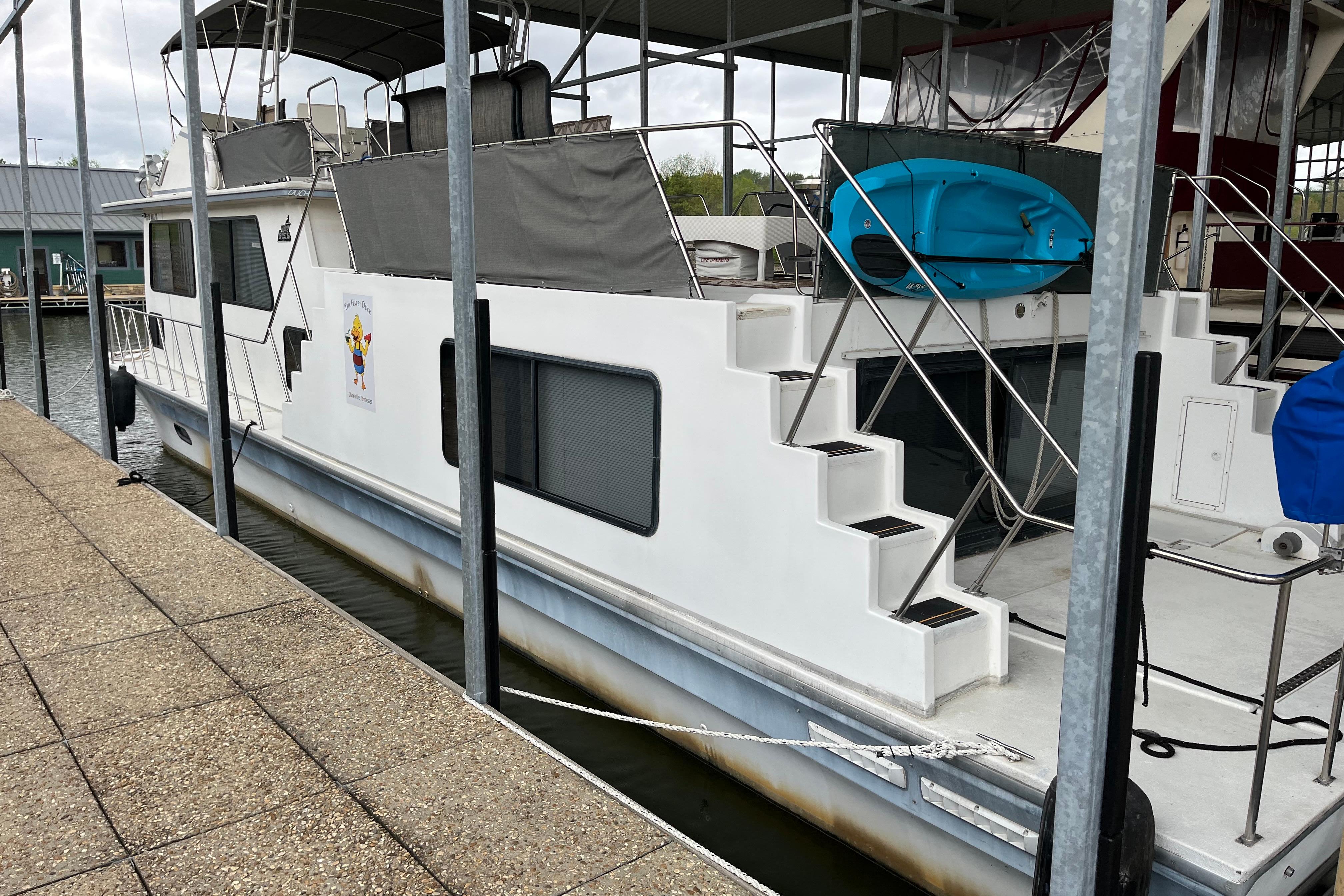 1995 WaveLenth Wide Body houseboat docked, featuring stairs and a blue kayak.