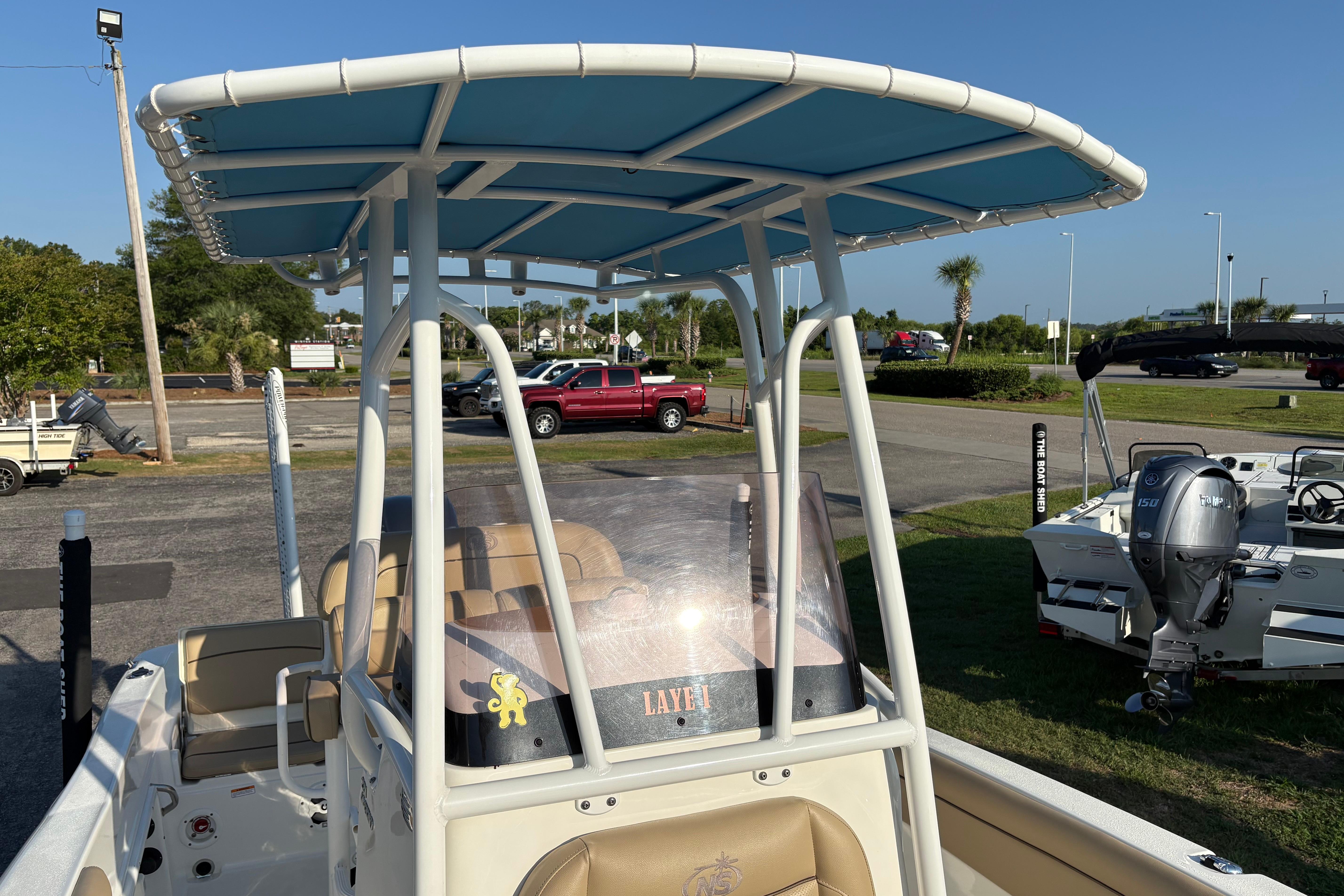 2019 NauticStar 231 Hybrid boat with blue canopy, parked outdoors.
