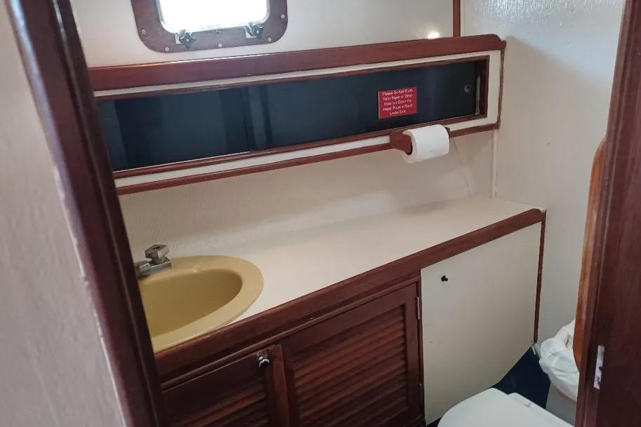 1977 Morgan Out Island 51 yacht bathroom with sink, wooden cabinetry, and porthole window.