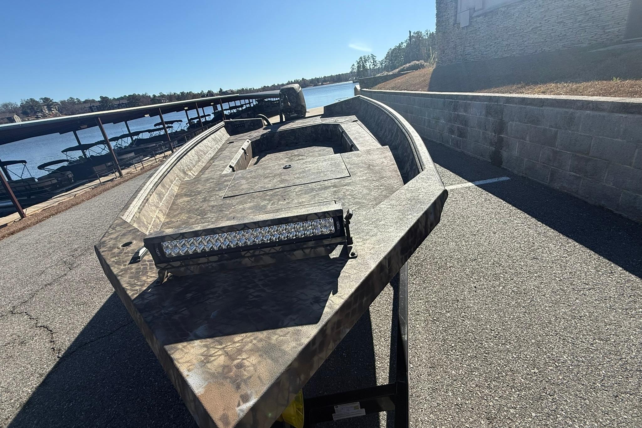 2026 Excel 183 Tomahawk boat with camouflage design, parked near a lakeside dock.