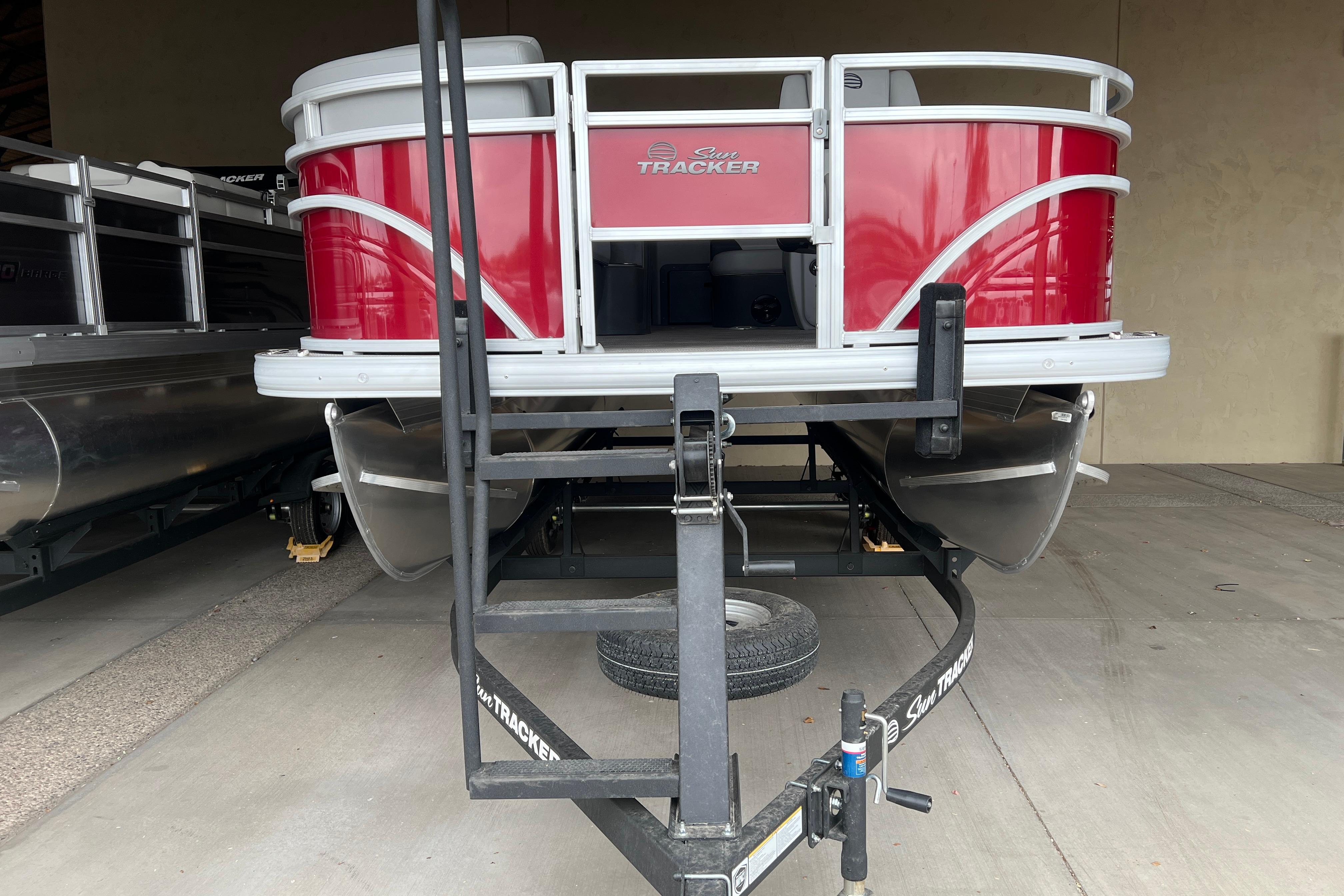 2026 Sun Tracker SportFish 20 DLX pontoon boat on trailer, red exterior, parked indoors.