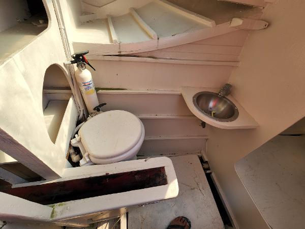 Compact bathroom in 1985 Crowther Buccaneer boat with toilet, sink, and fire extinguisher.