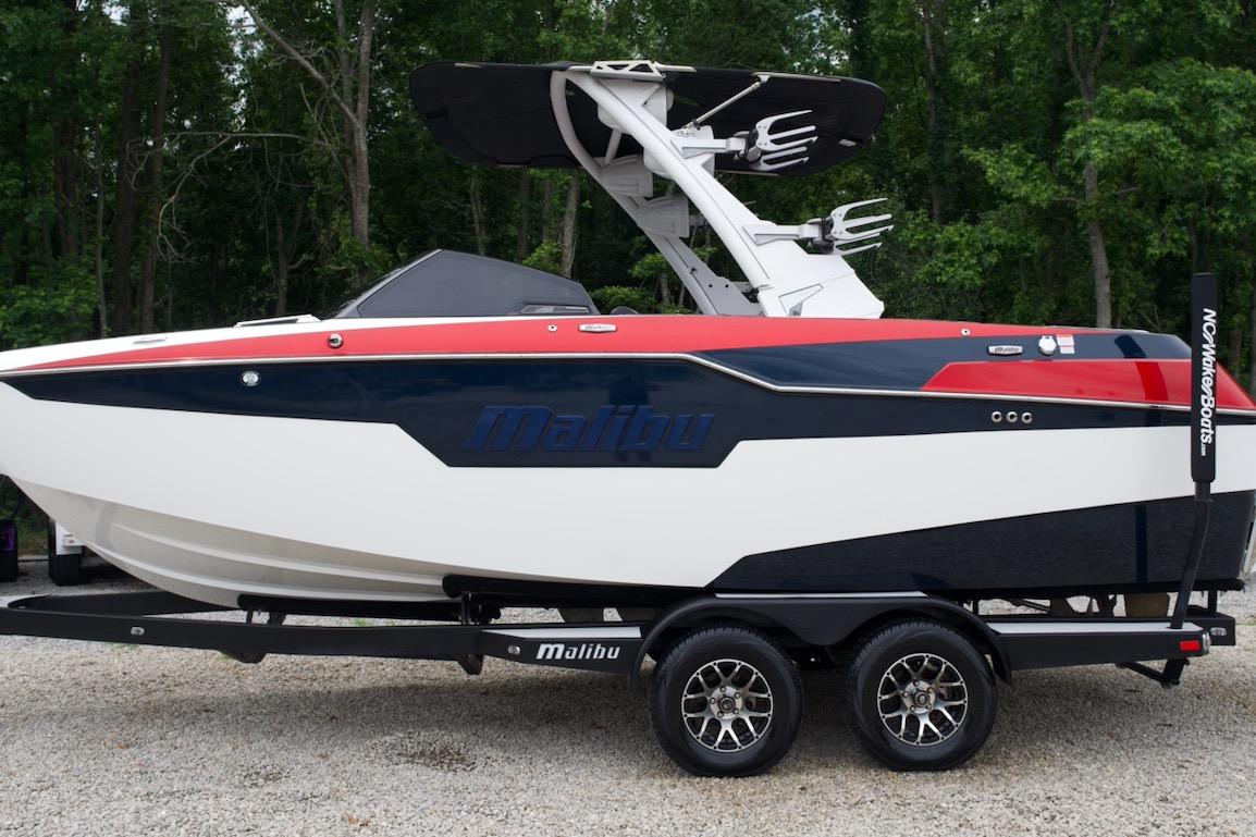 2021 Malibu M220 boat on trailer, sleek design, red and blue accents, forest background.