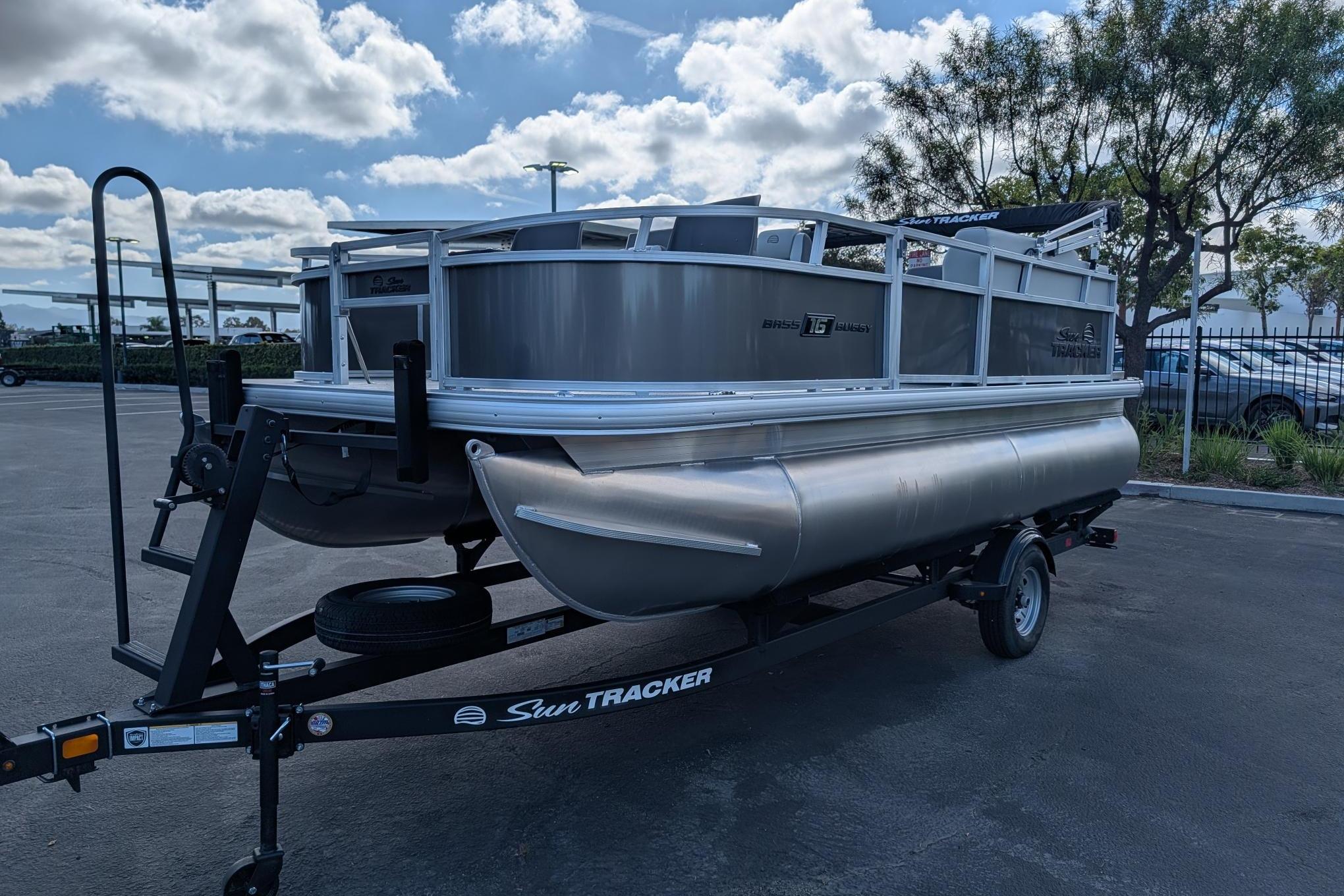 2026 Sun Tracker Bass Buggy 16 XL Select pontoon boat on trailer, parked outdoors.