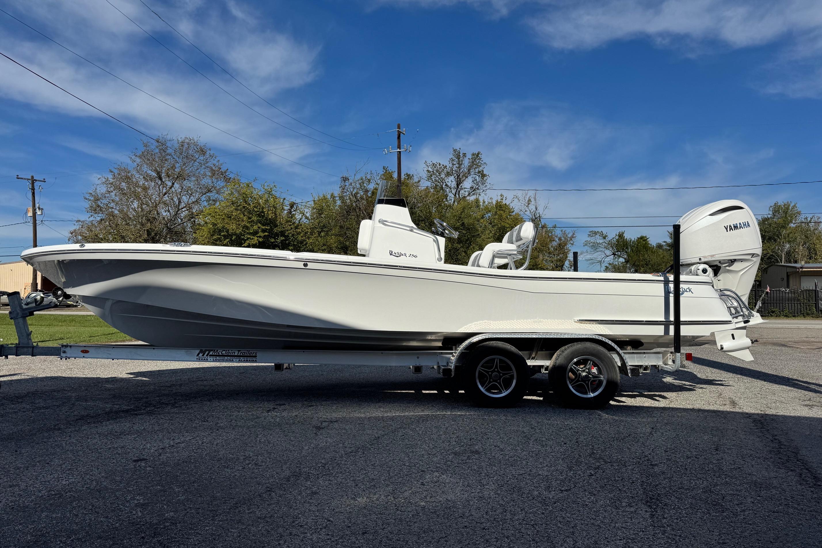 2026 BlackJack 256 Bay boat on trailer, parked outdoors under clear blue sky.