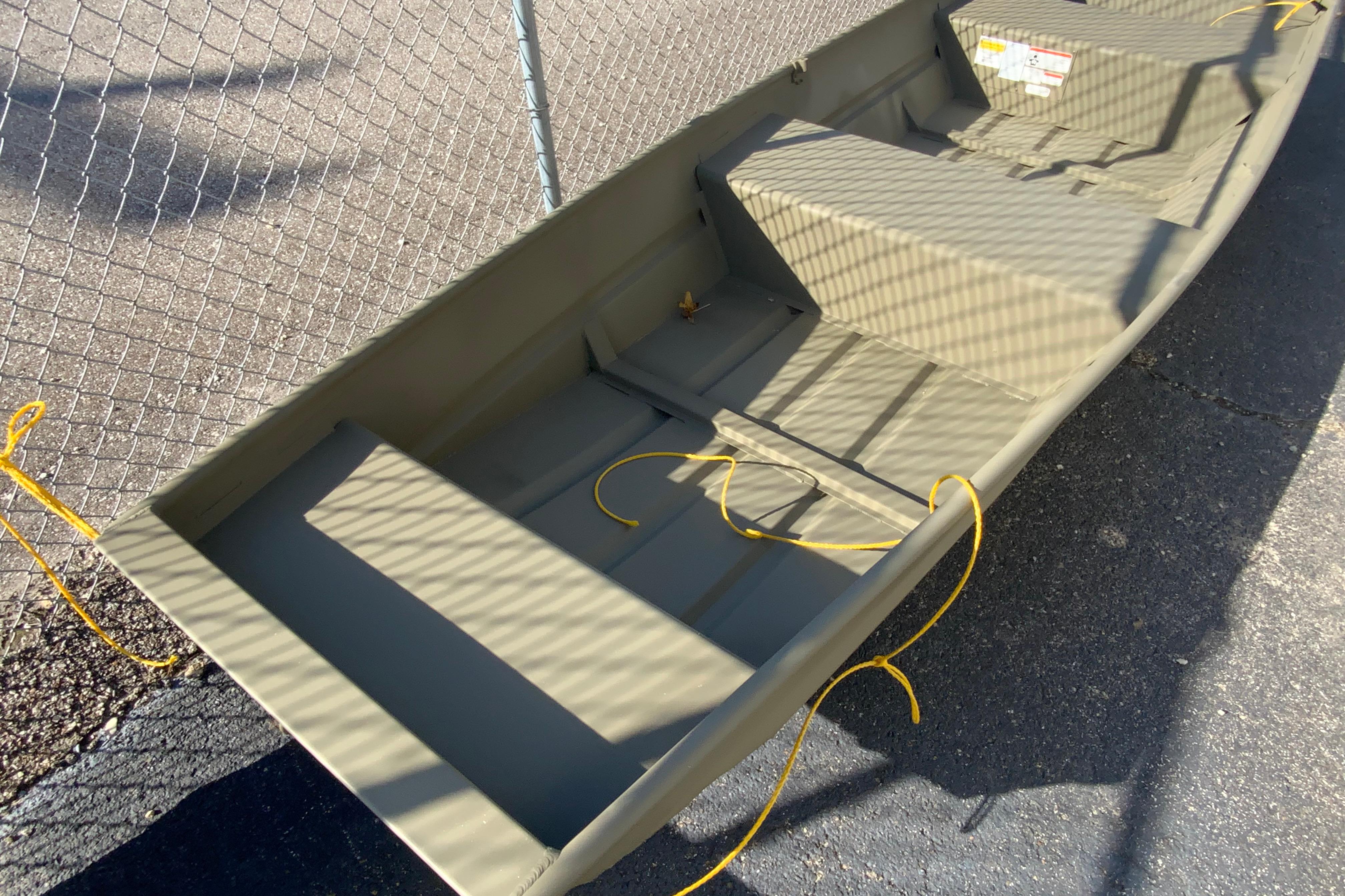 2026 Tracker Grizzly 14 Jon boat, olive green, parked on asphalt near chain-link fence.