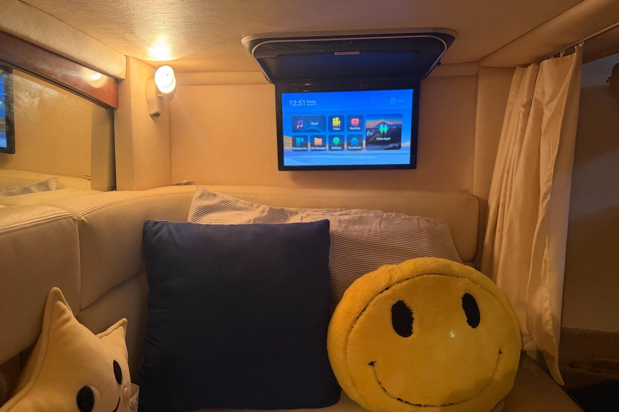 Cozy cabin interior of 2002 Sea Ray Sundancer 320 with TV and smiley pillow.