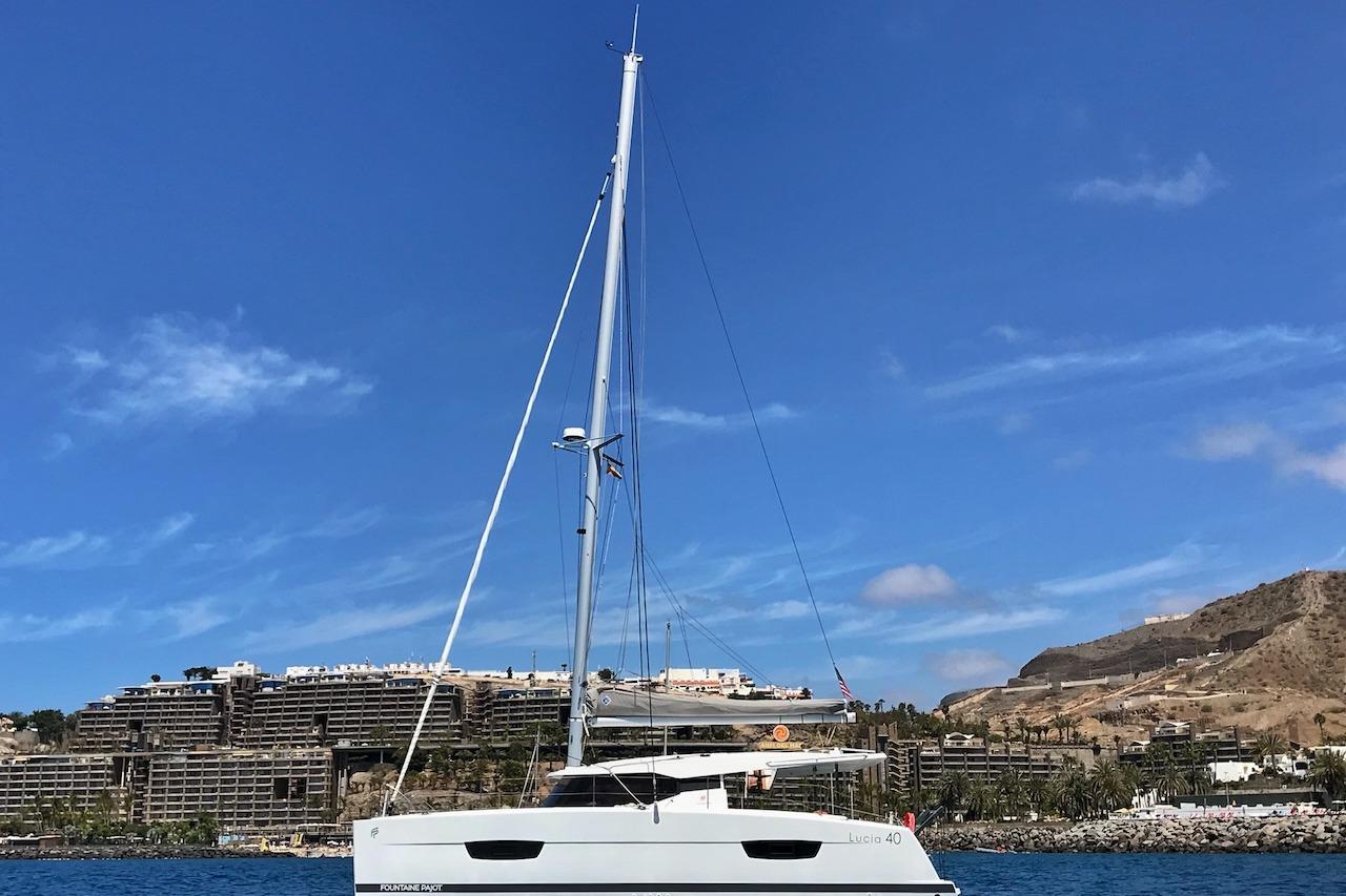 2018 Fountaine Pajot Lucia 40 catamaran sailing near coastal buildings under clear blue sky.