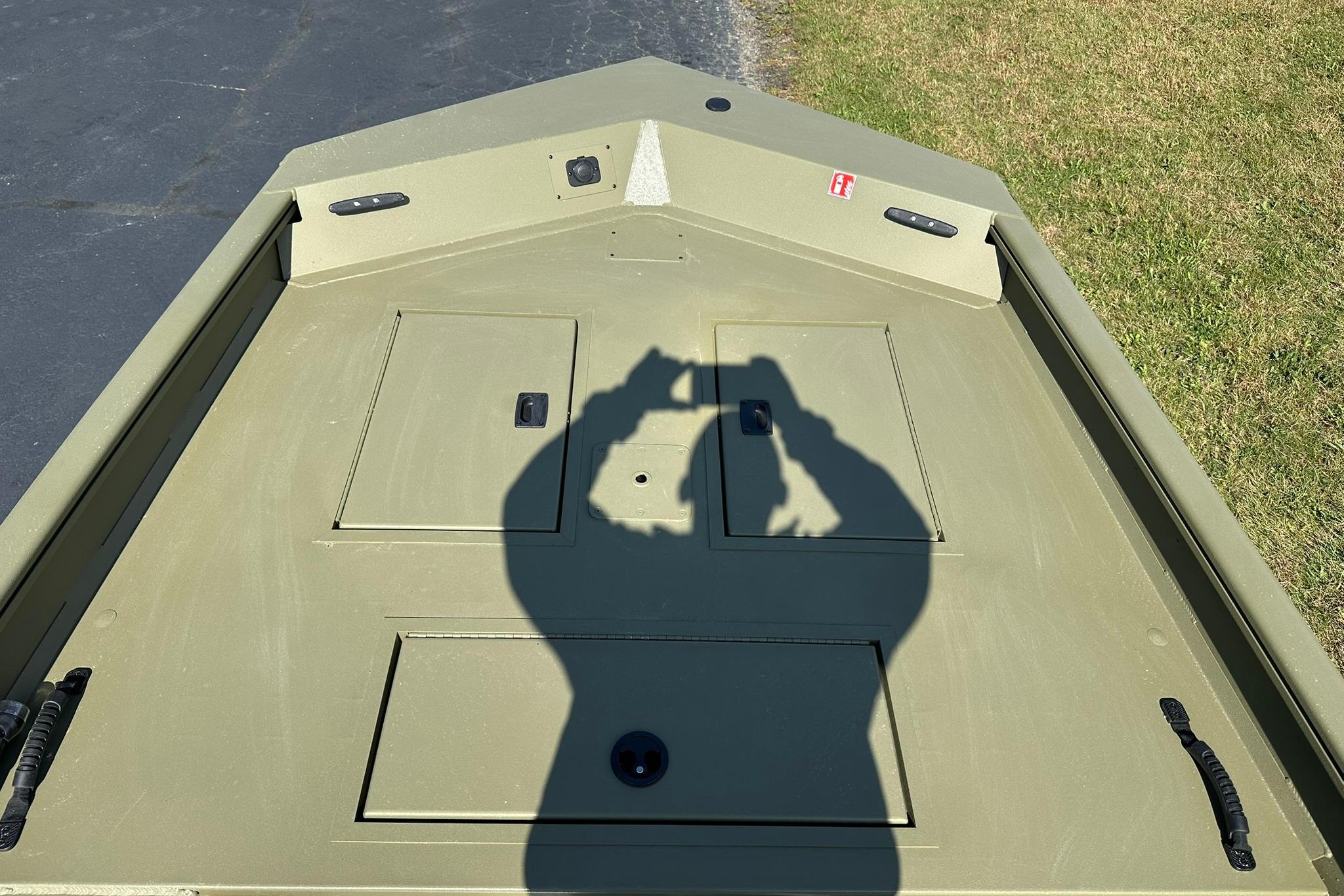 2026 Lowe Roughneck 1860SC boat deck with shadow, parked on grass and pavement.