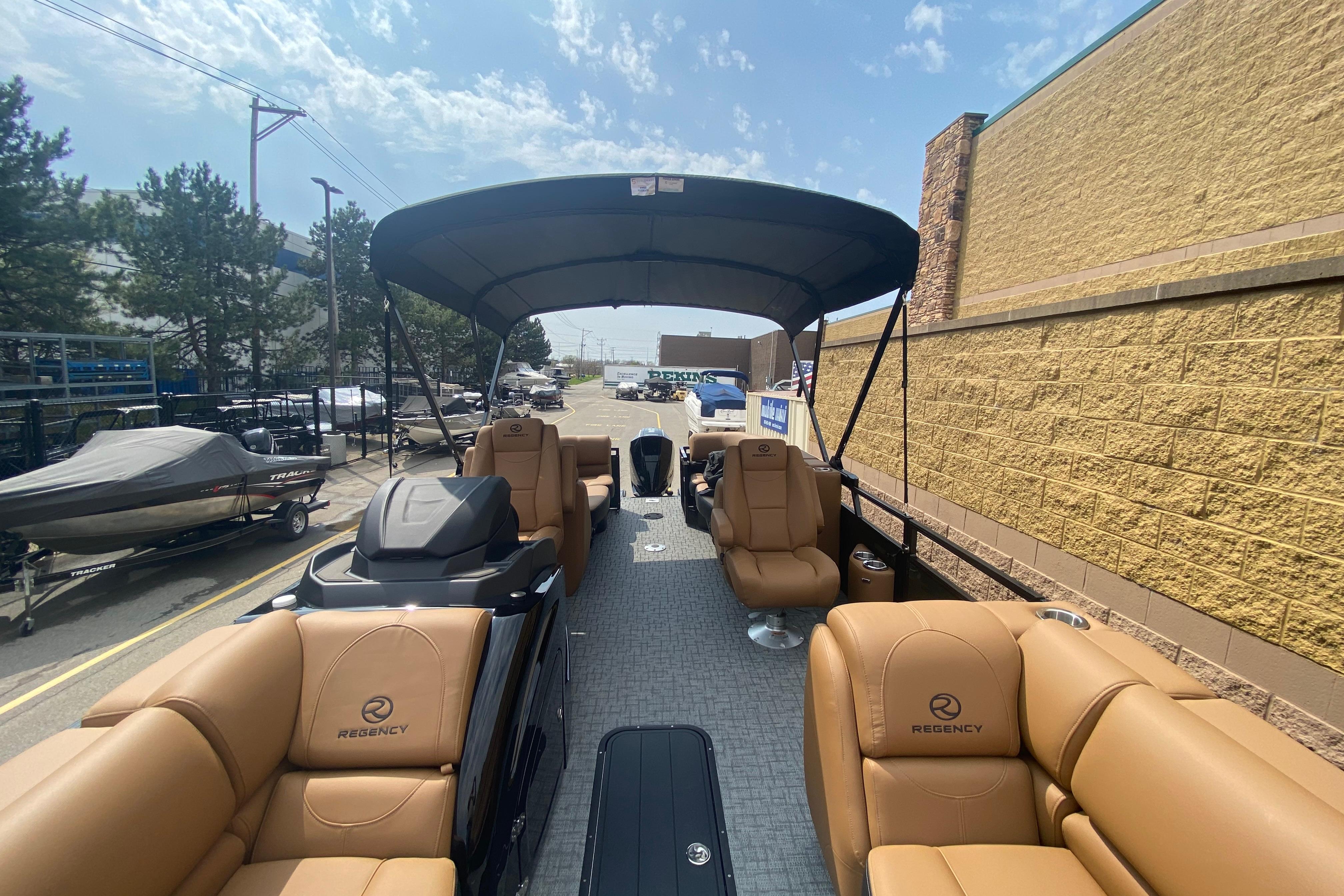 2026 Regency 230 DL pontoon boat with tan seating and canopy, parked outdoors.