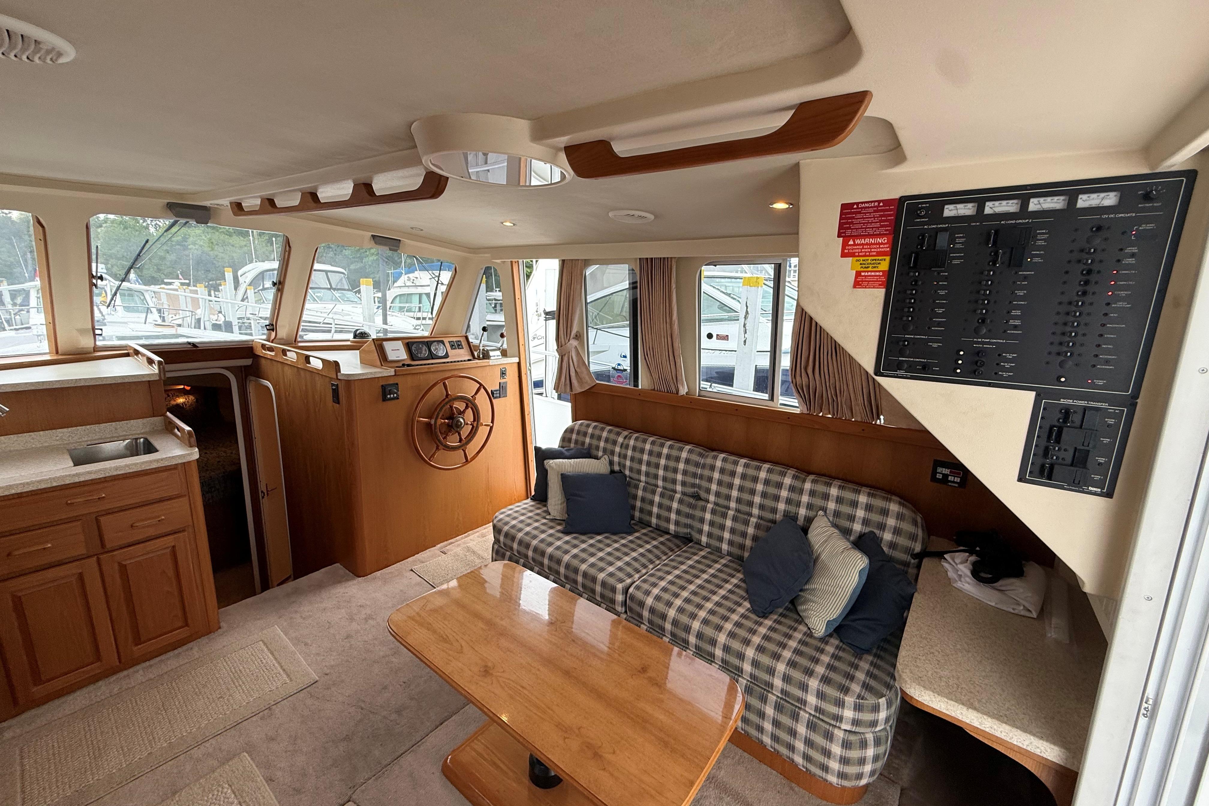 Interior of 1999 Mainship 350 Trawler with helm, plaid sofa, and control panel.