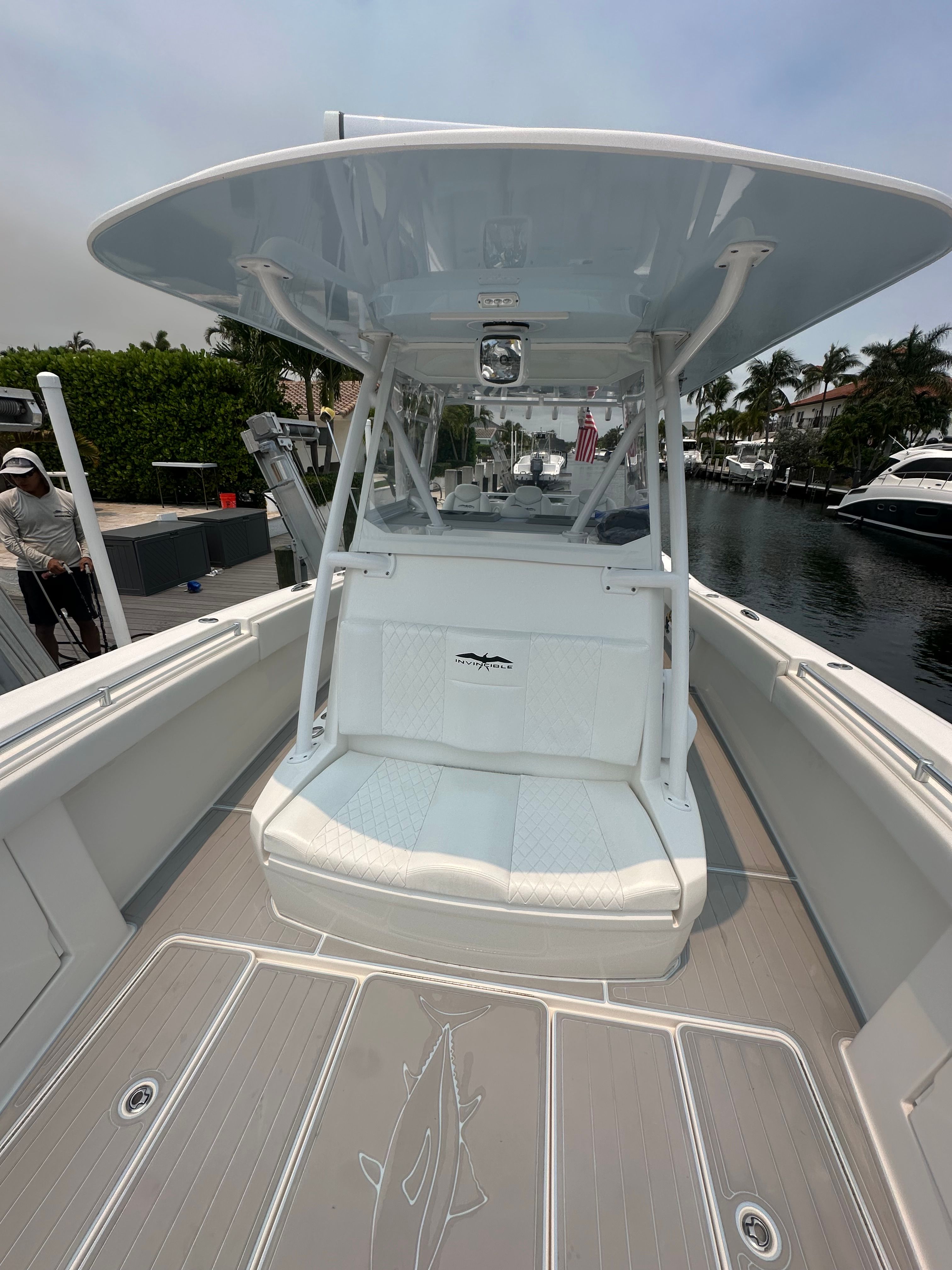 A modern boat with a covered helm and seating area, docked in a calm canal.