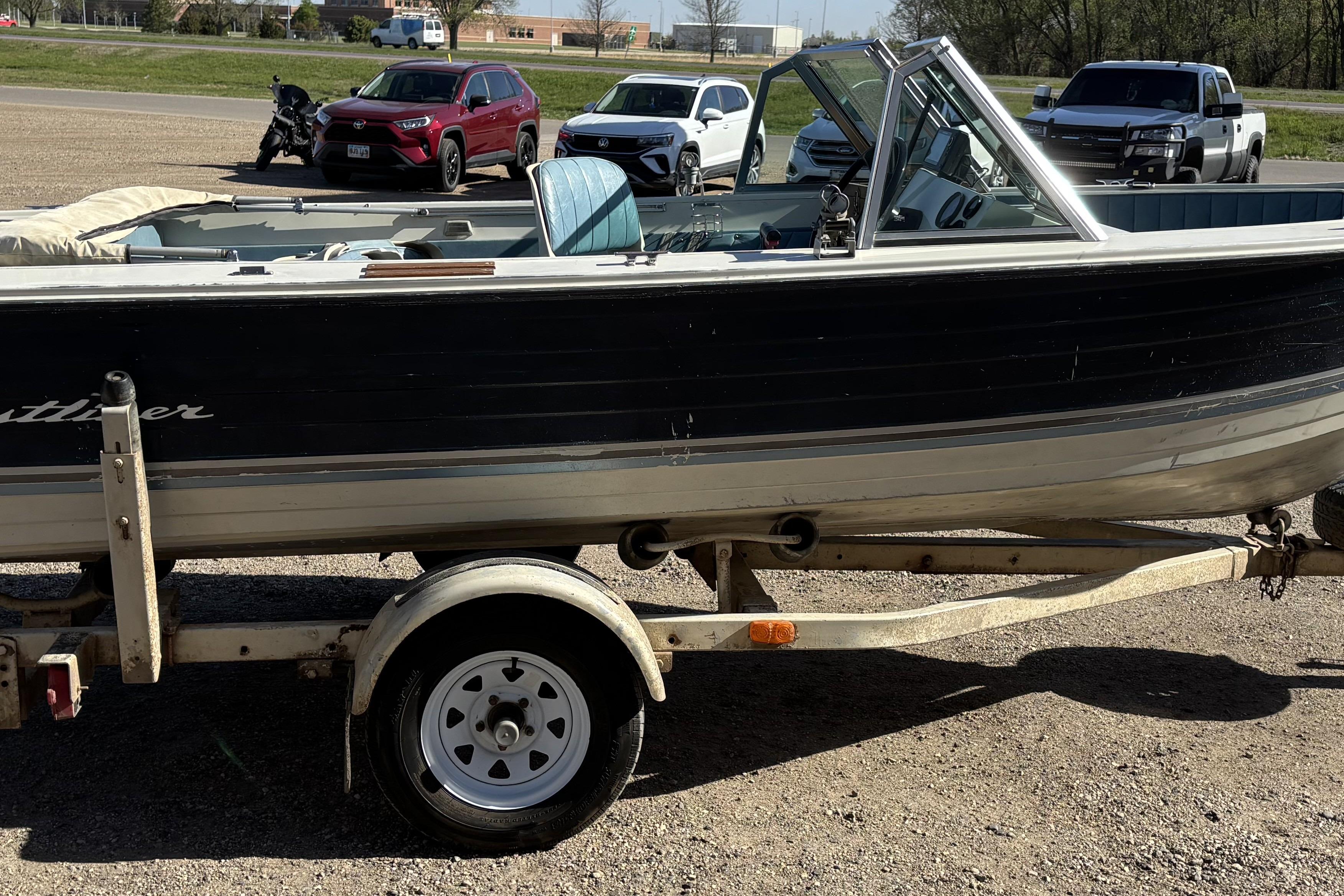 1983 Crestliner 16 boat on trailer, parked in a lot with cars and motorcycle nearby.