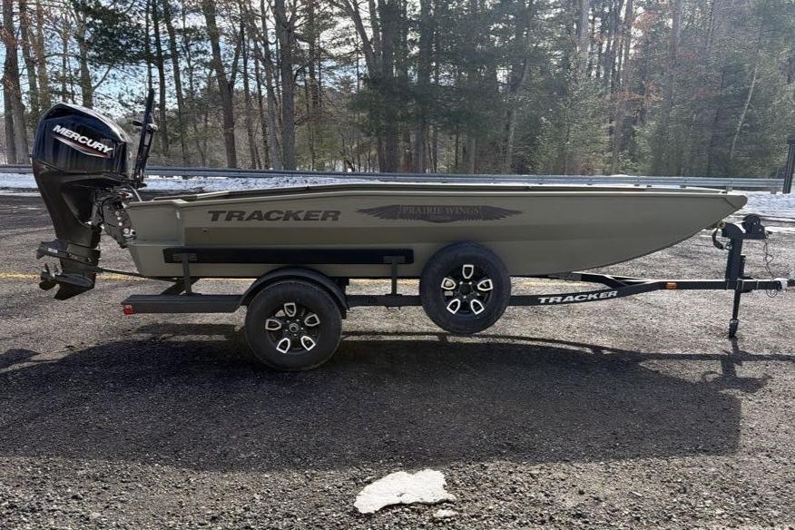 2026 Tracker Grizzly 1650 T Prairie Wings Edition boat on trailer in wooded area.