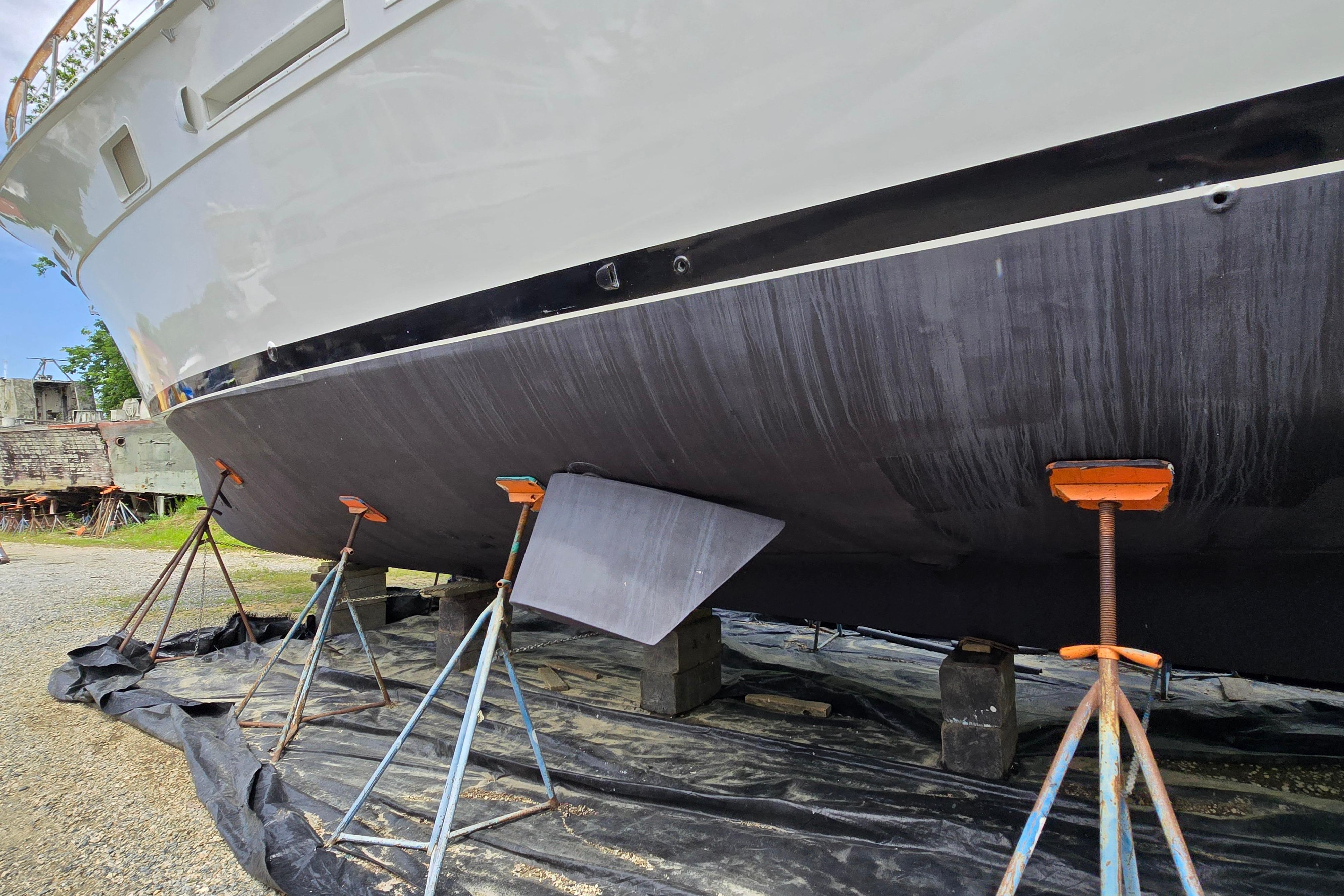 1980 Hatteras 70 Motor Yacht on stands, hull view, in a boatyard setting.
