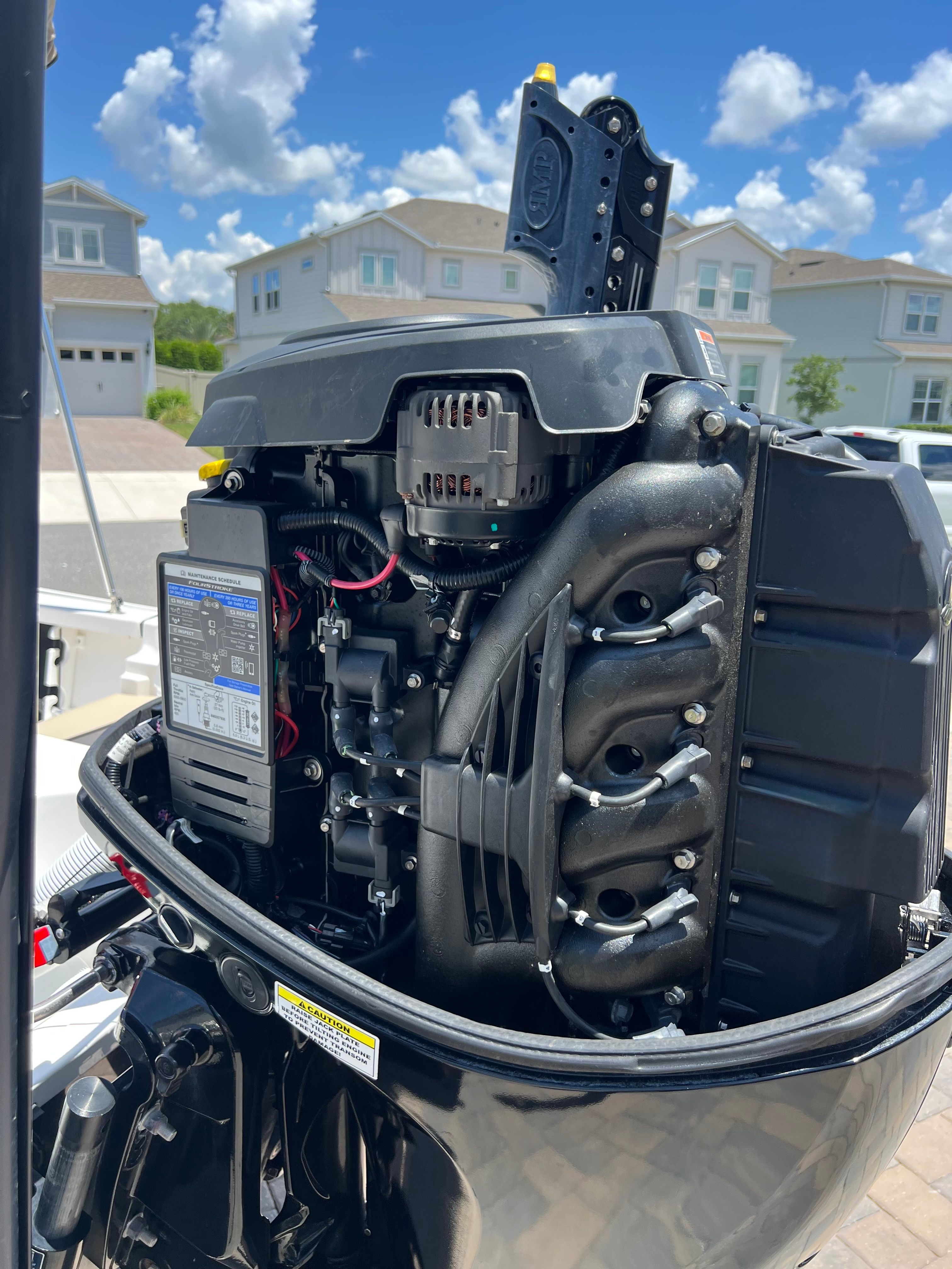 An outboard motor of a boat with exposed components, surrounded by houses in the background.