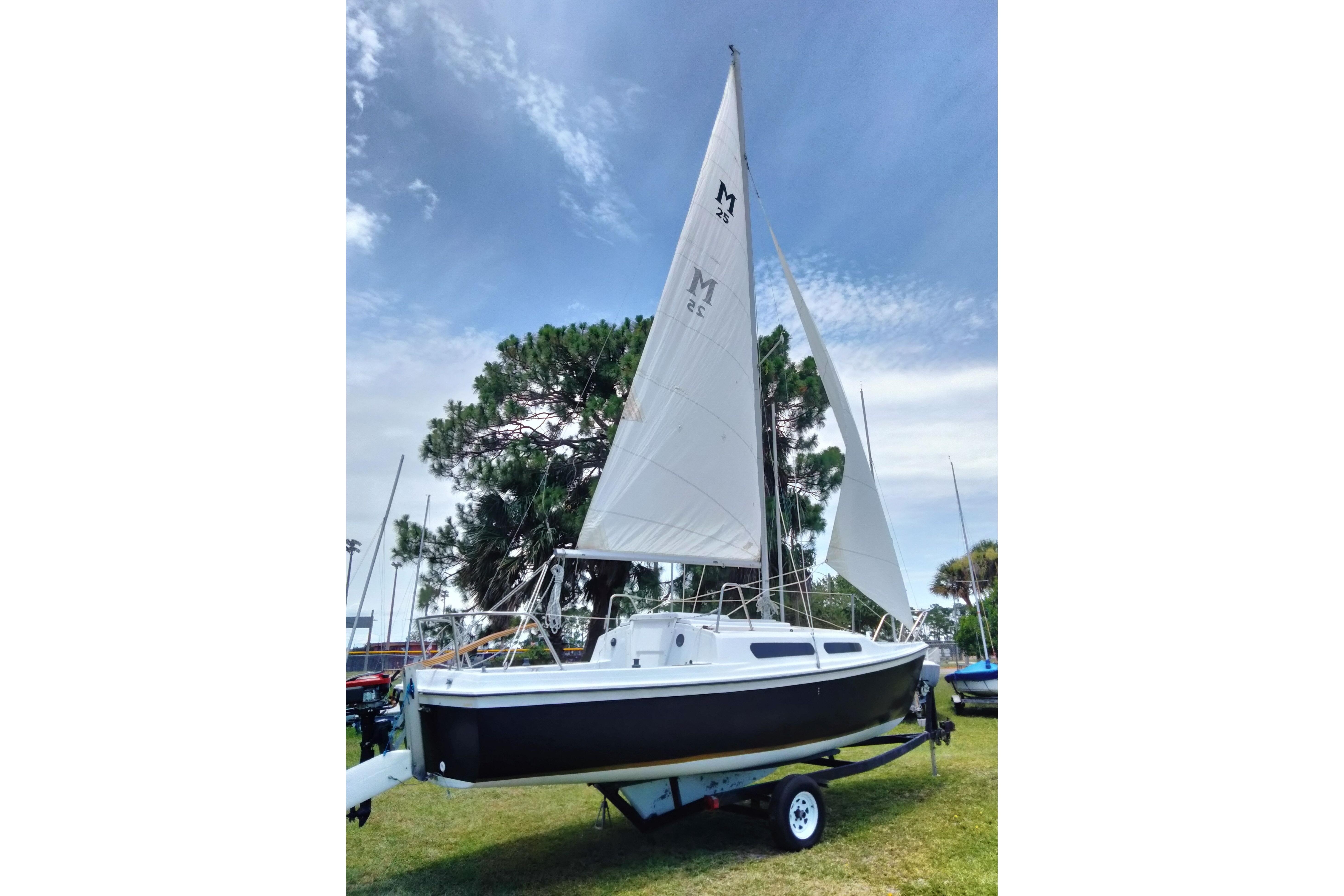 1980 MacGregor 25 sailboat on trailer, set against a clear sky and trees.