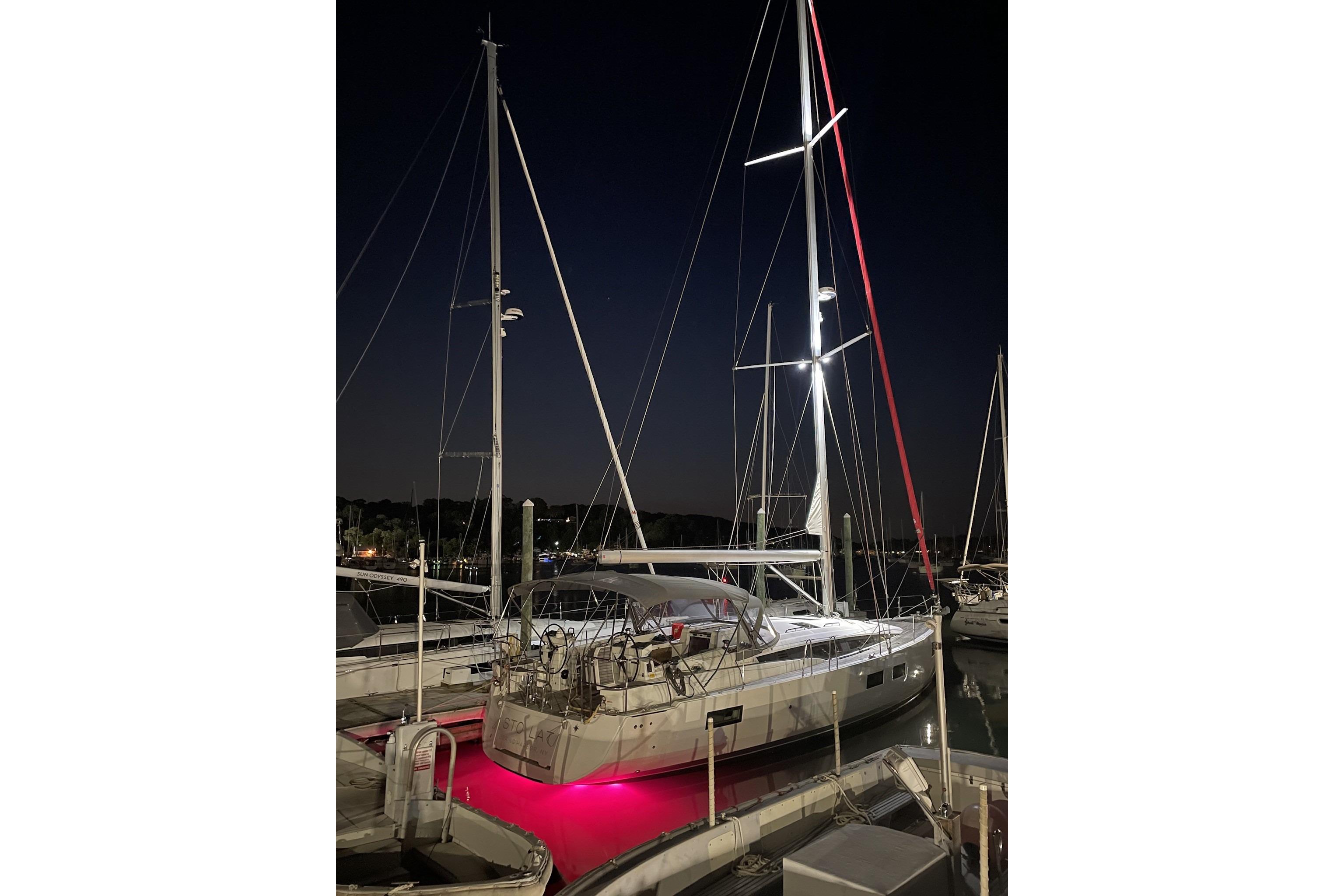 2018 Jeanneau 51 sailboat docked at night with vibrant red underwater lights.