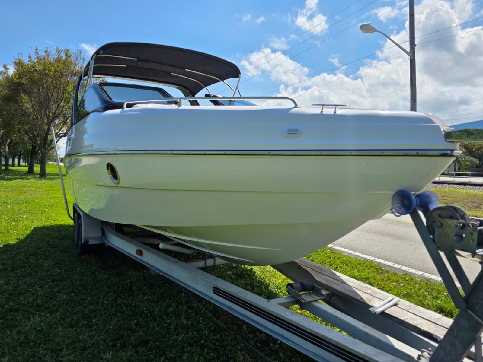 A 2025 Coral 26 boat on a trailer, surrounded by grass and trees.