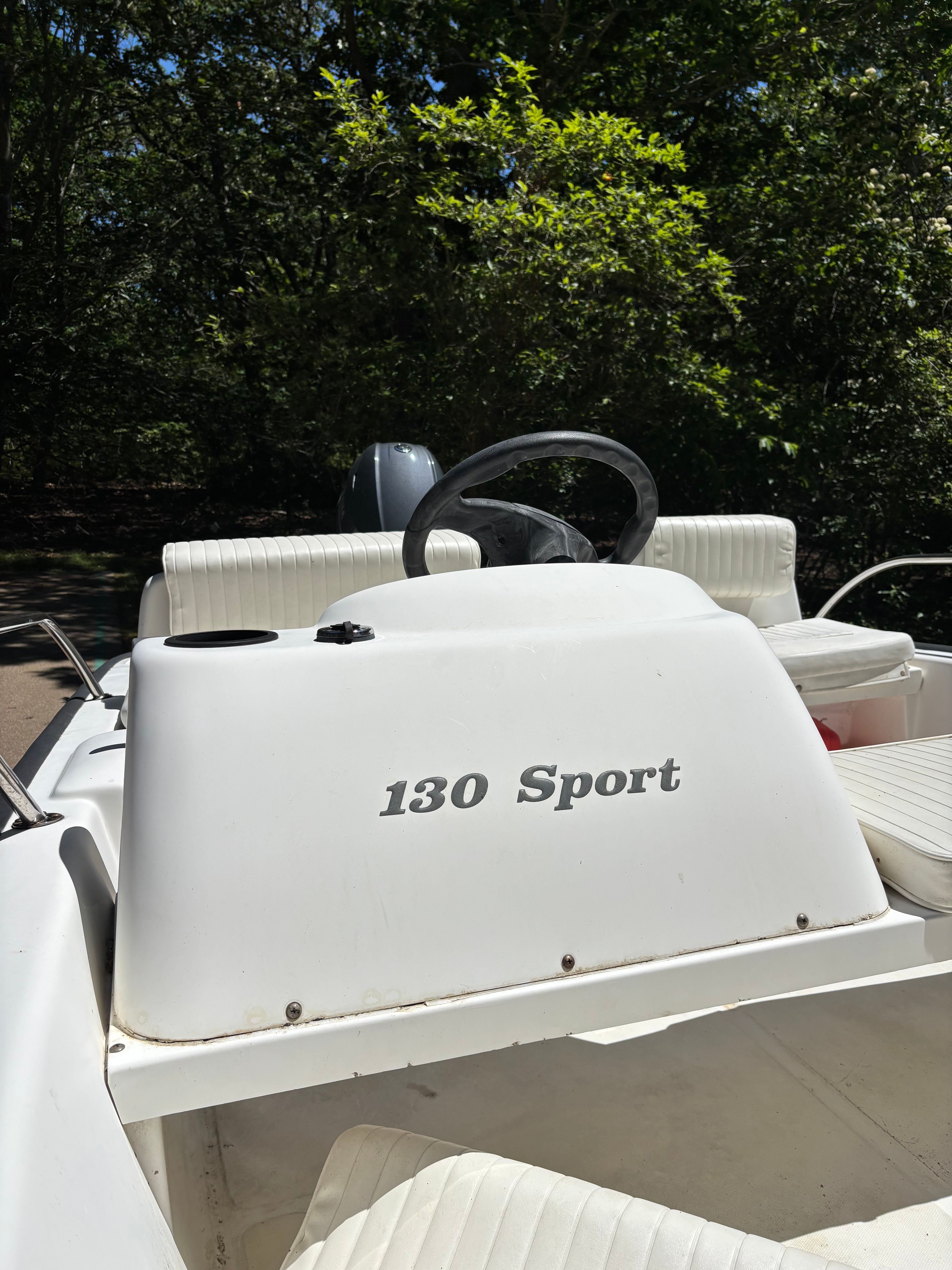 The boat has white seats and a steering wheel, surrounded by trees.