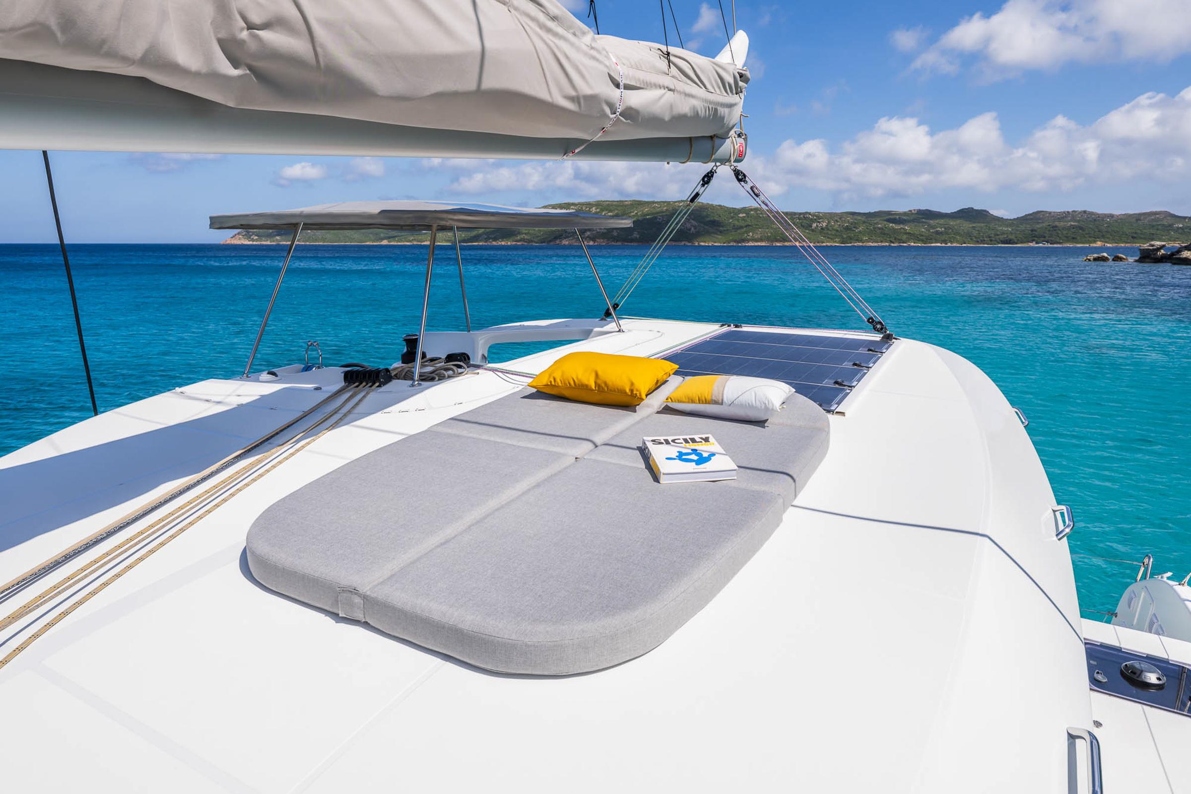 2025 Lagoon 38 catamaran with sunbathing area, cushions, and book, anchored in turquoise waters.