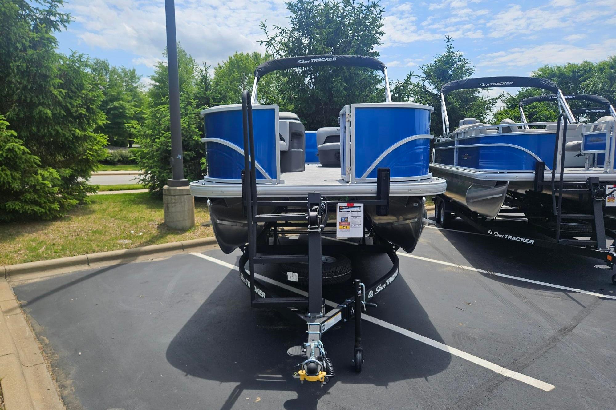2026 Sun Tracker Party Barge 18 DLX pontoon boat in parking lot, surrounded by trees.
