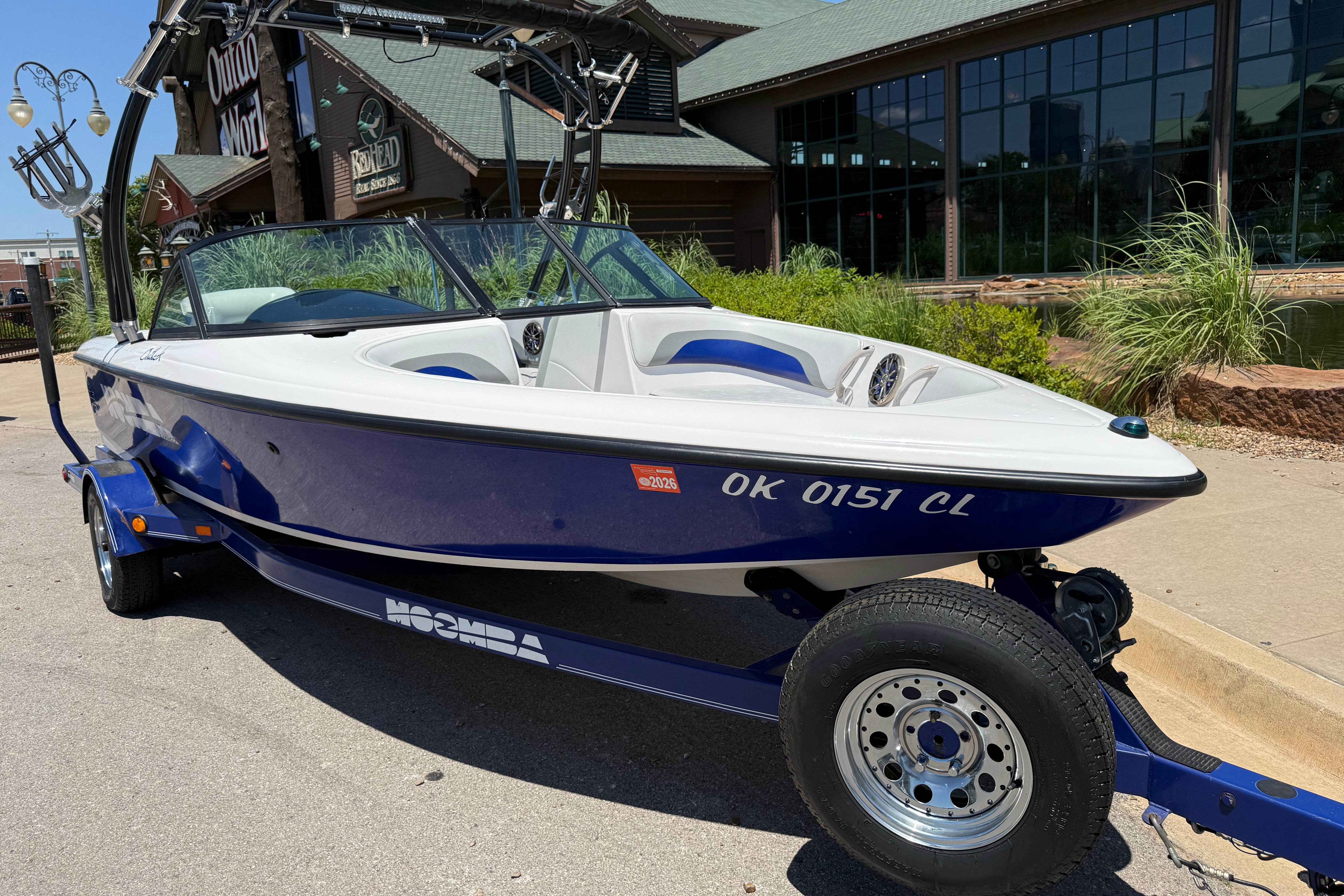 2001 Moomba Outback boat on trailer, parked outside a building on a sunny day.