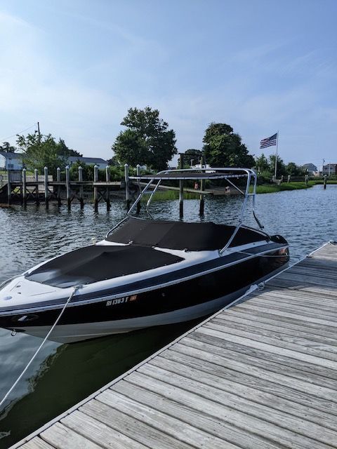 A 2003 Cobalt 240 boat is docked at a wooden pier. It has a black canopy and a flag waves in the background.