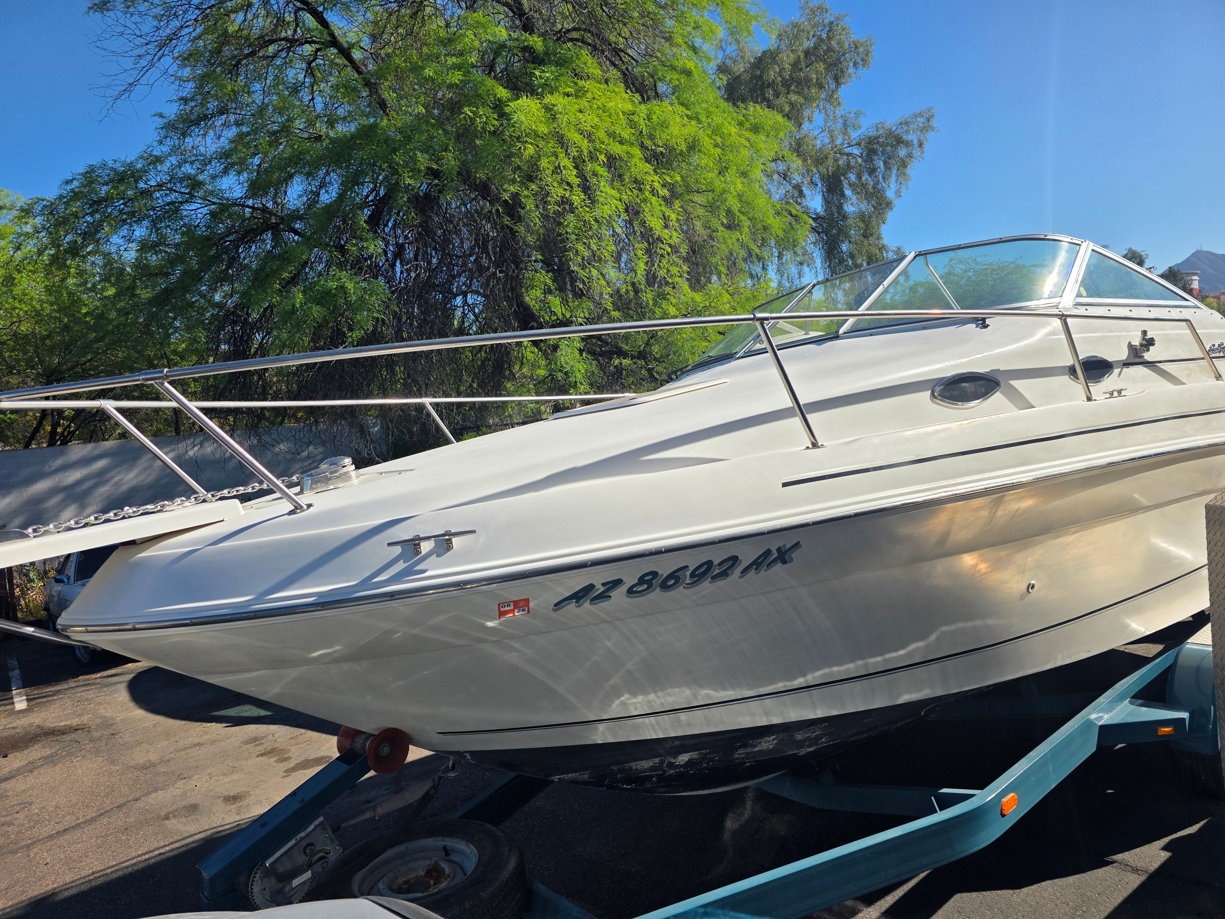 A 1997 Sea Ray 240 Sundeck boat on a trailer, surrounded by trees.