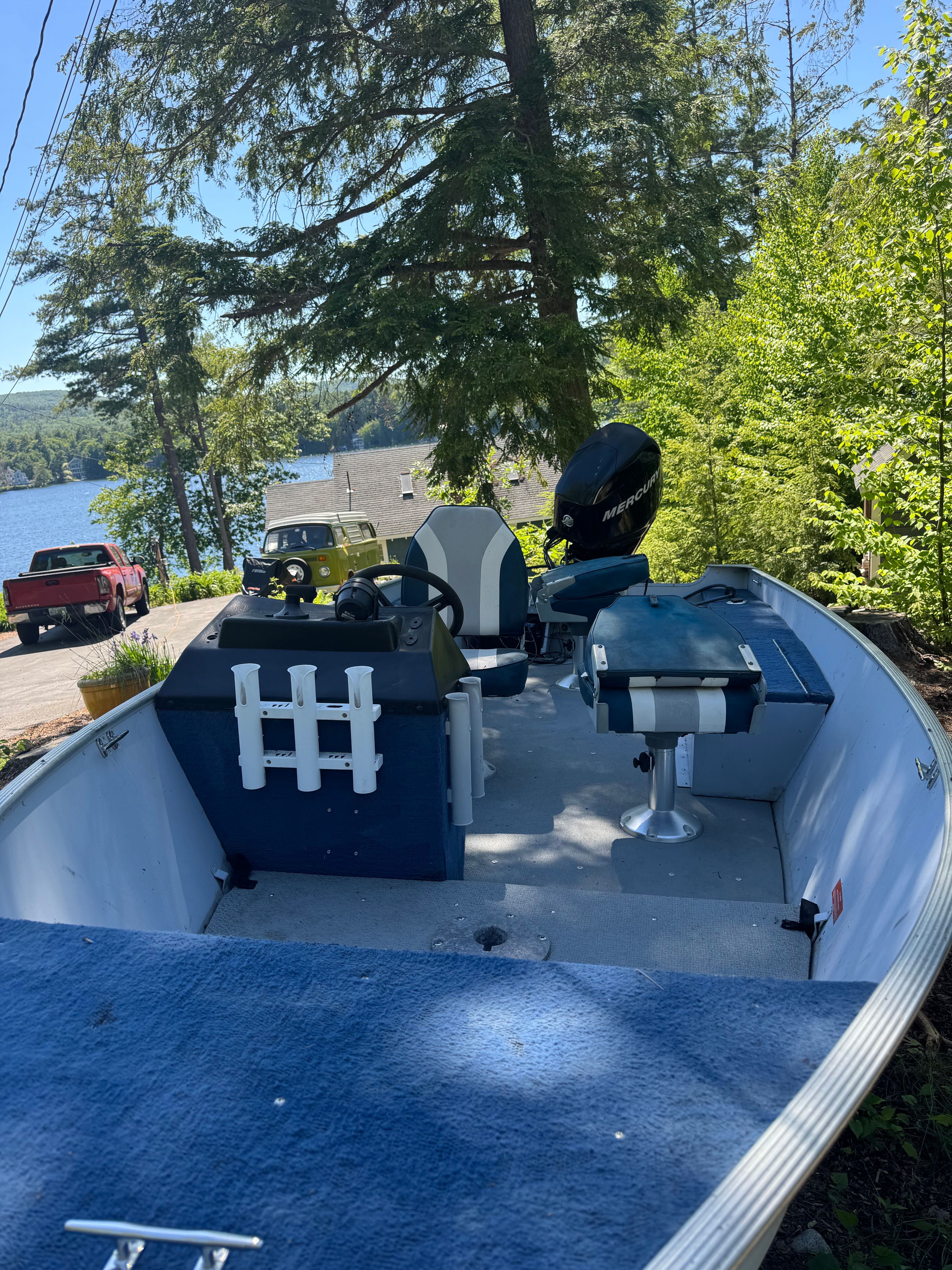 A boat is on a trailer in a wooded area near a lake.