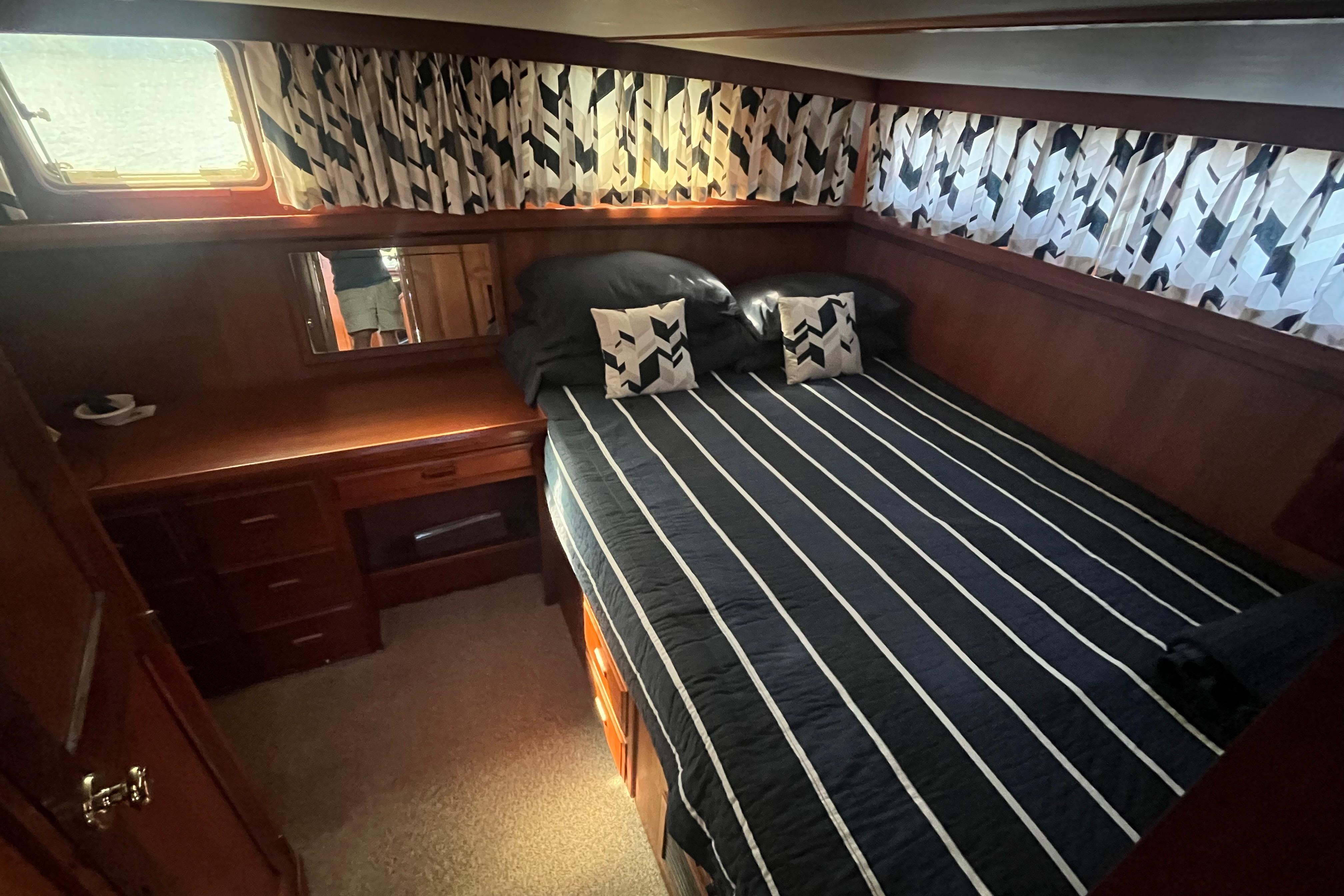 Cozy bedroom in 1990 Cooper Prowler 35 yacht with striped bedding and wooden furnishings.