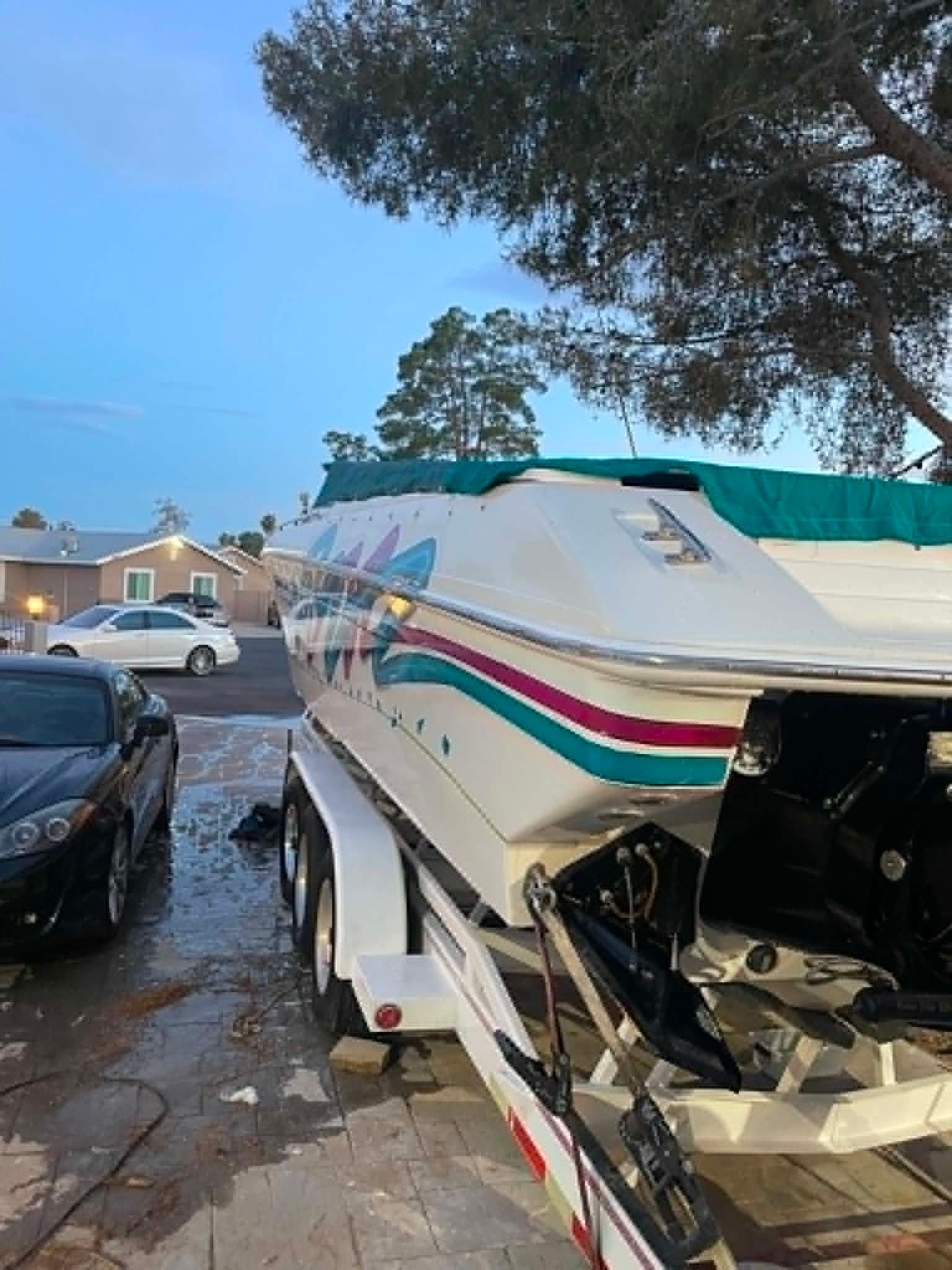A white speedboat with colorful stripes sits on a trailer in a driveway.