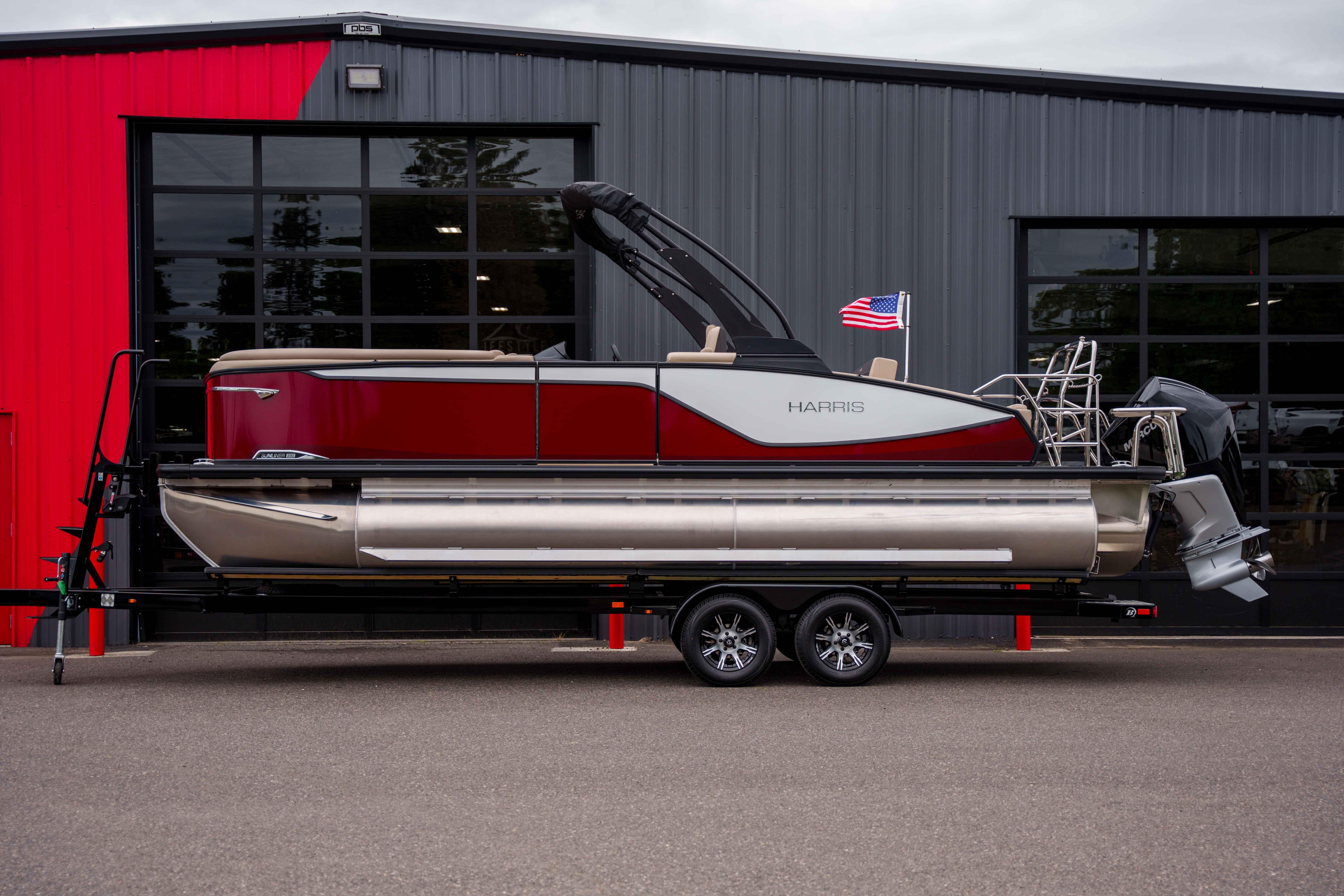 2026 Harris Sunliner 230 pontoon boat on trailer, parked outside a modern building.