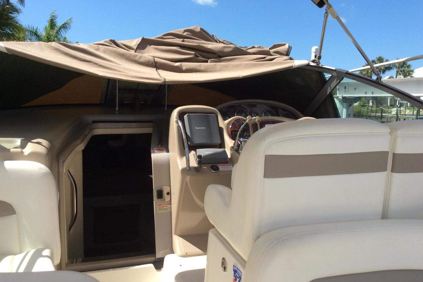 2003 Sea Ray 320 Sundancer cockpit with beige seating and navigation equipment under a canopy.