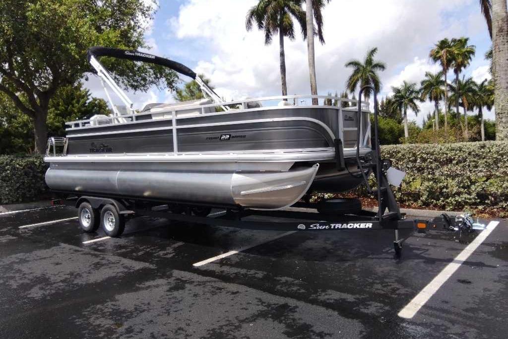 2026 Sun Tracker Fishin' Barge 22 DLX pontoon boat on trailer in parking lot.