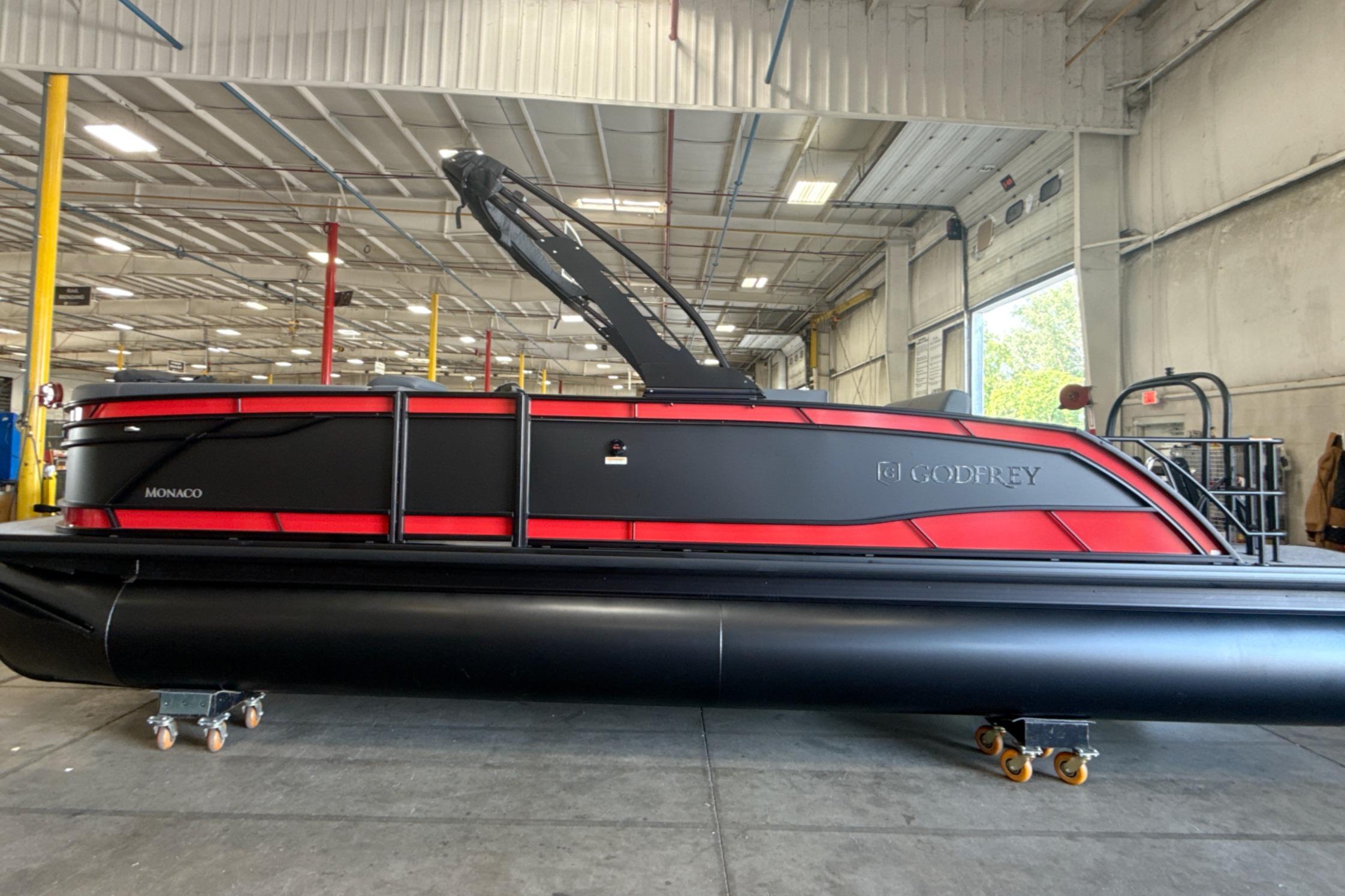 2027 Godfrey Monaco 25' Tritoon in warehouse, sleek black and red design.