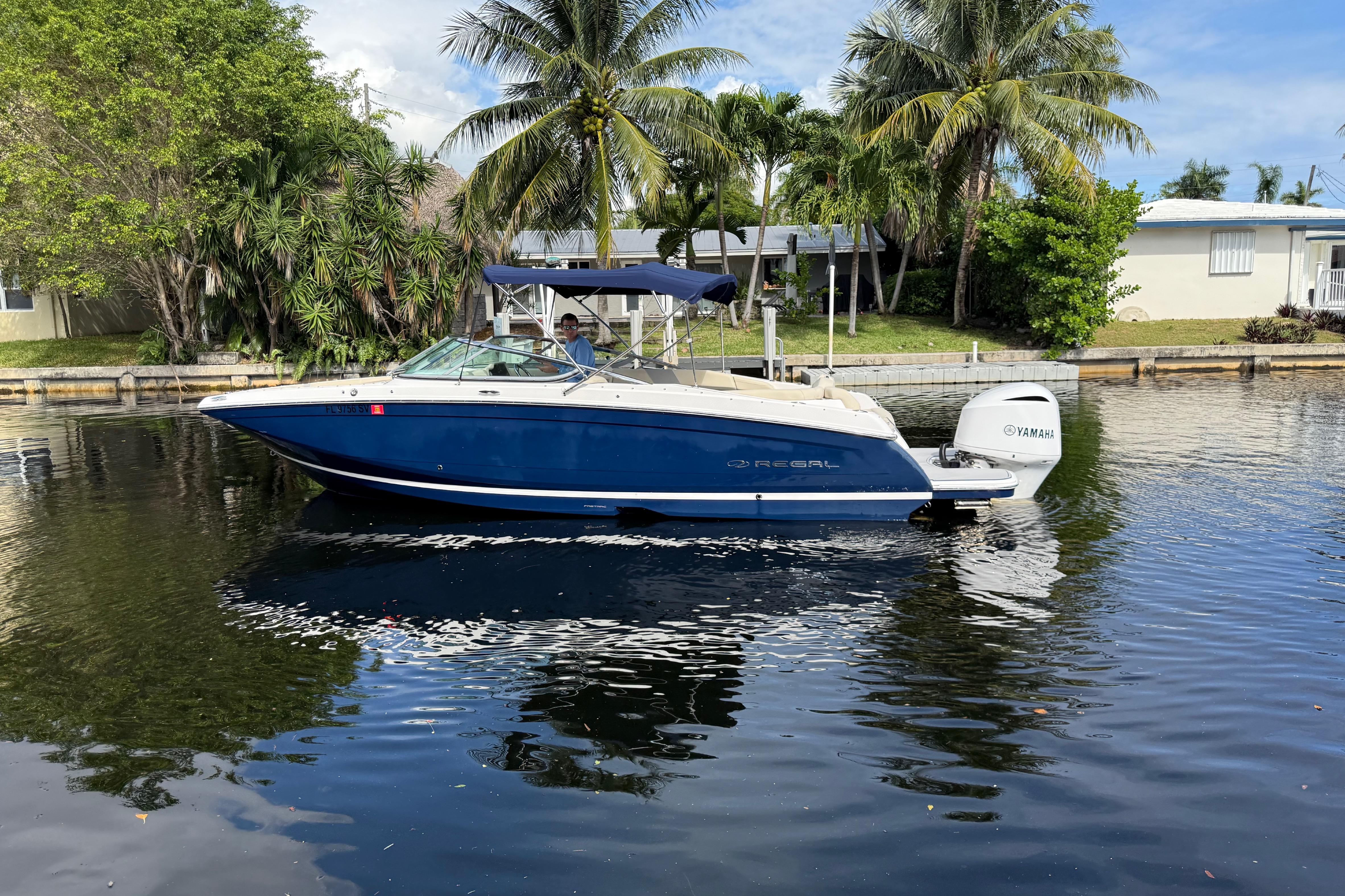 2021 Regal 26 OBX boat on calm water, surrounded by palm trees and houses.