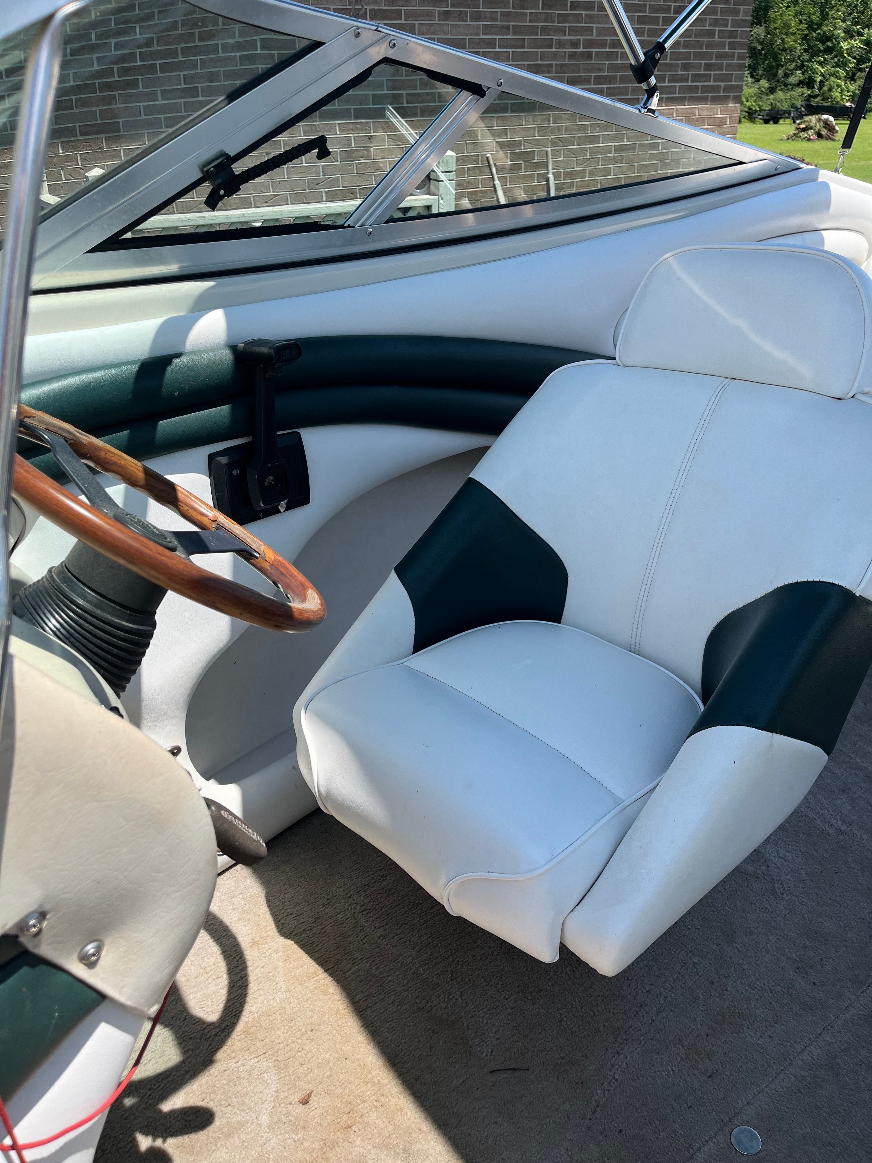 Interior of a 1996 Crownline 202 BR with white and green seat and wooden steering wheel.