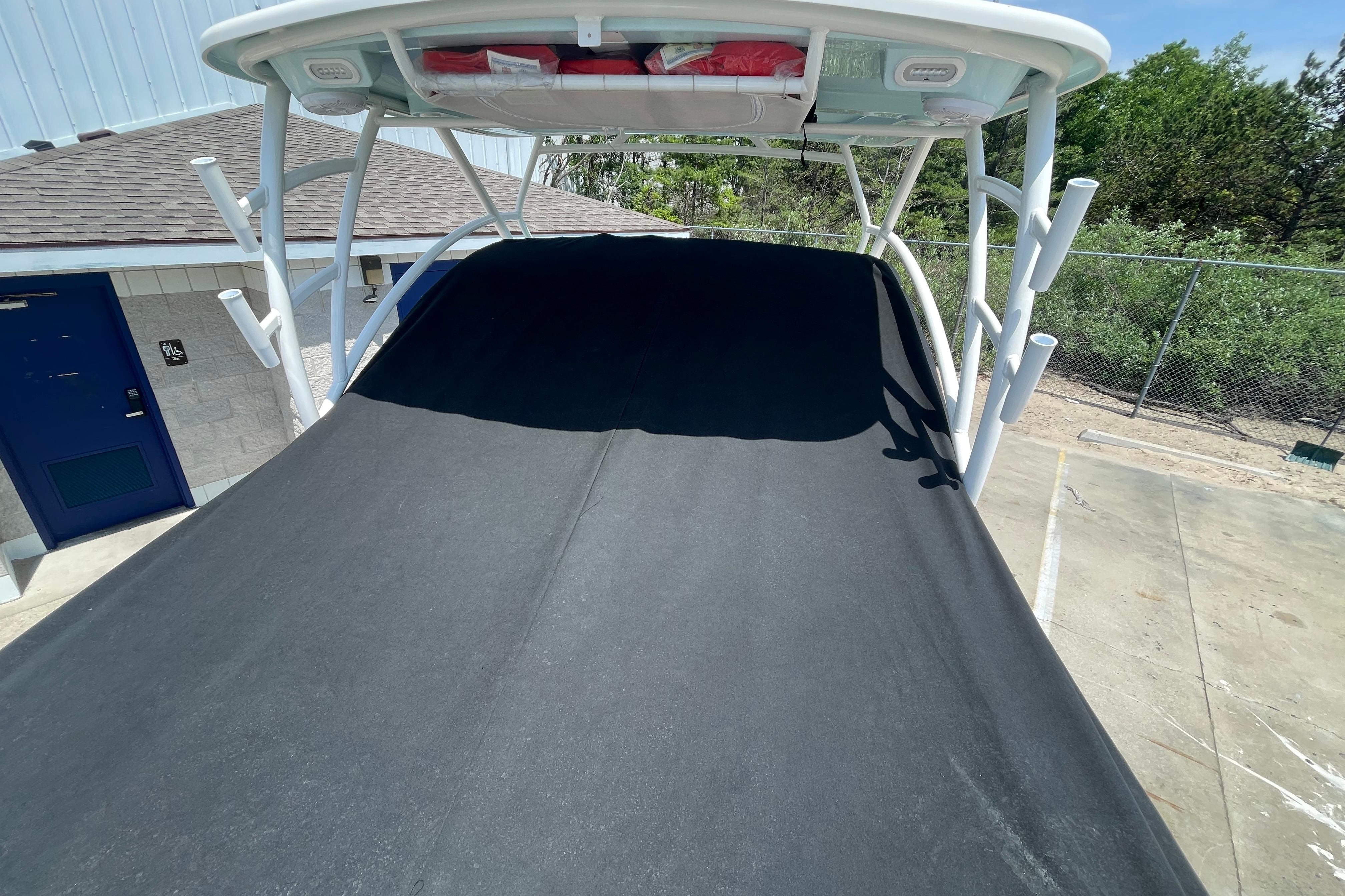 2022 Sailfish 245 DC boat with black cover, docked near a building and trees.
