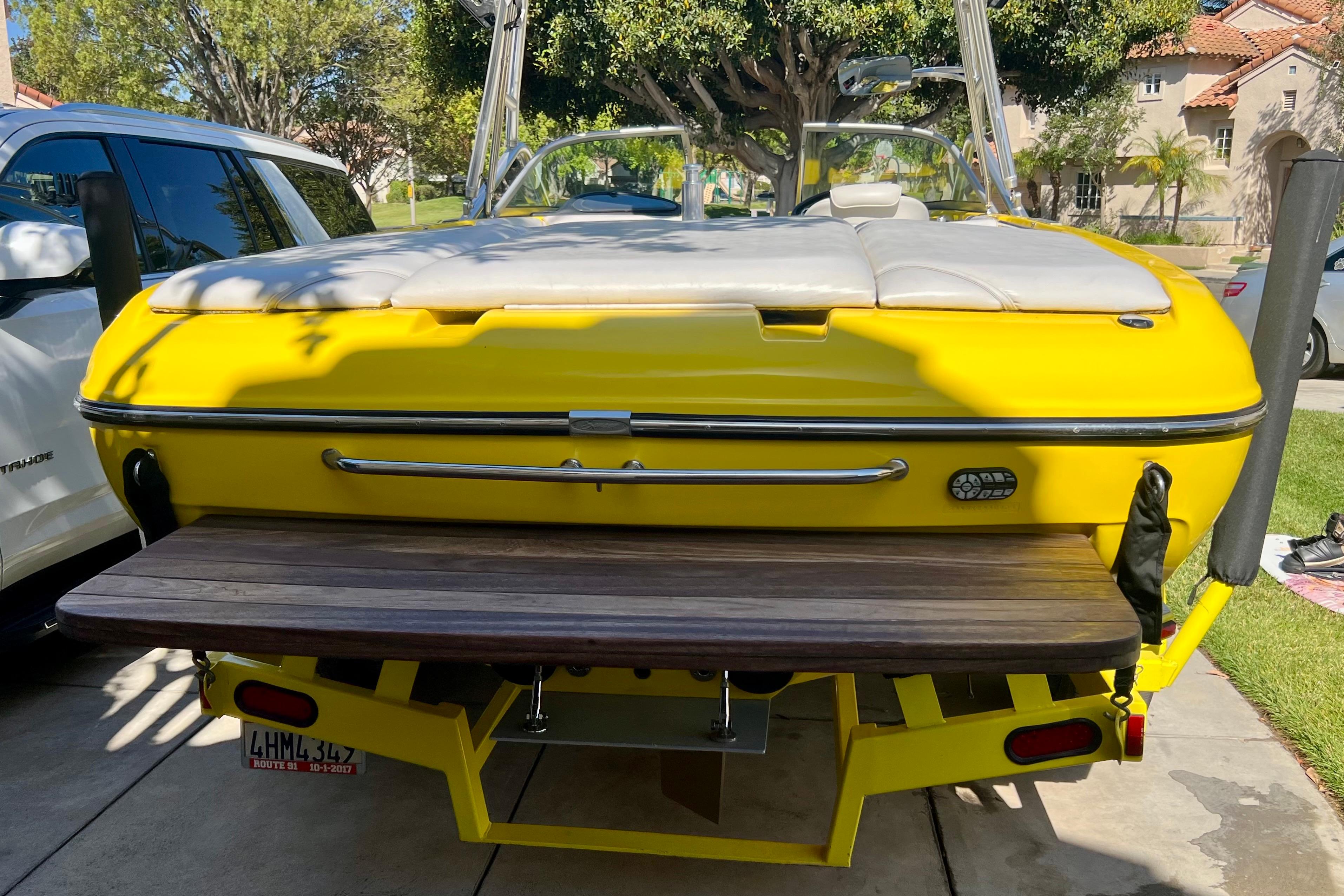 Yellow 2006 Sanger V230 boat parked on driveway, featuring a wooden swim platform.