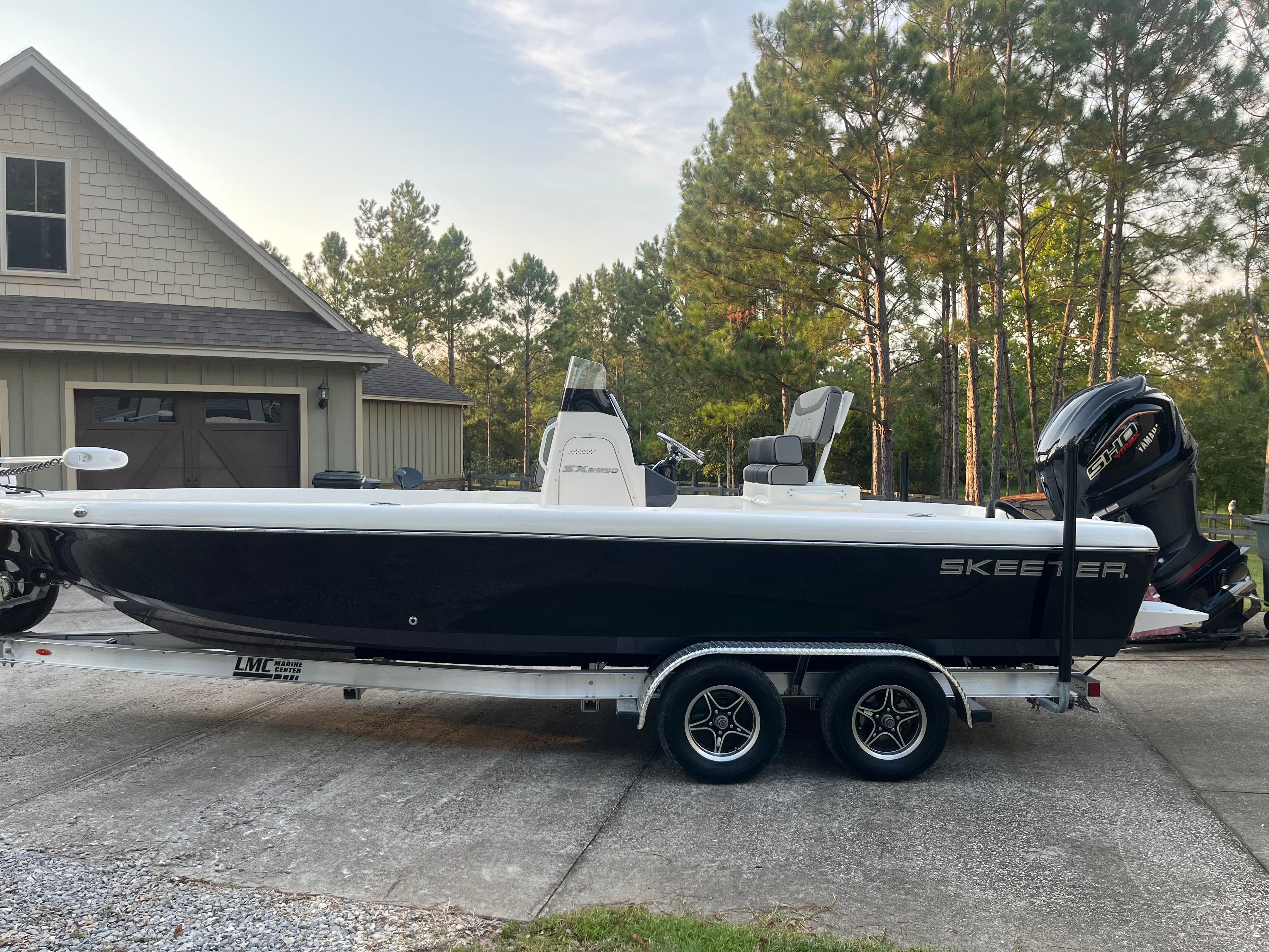 A 2023 Skeeter SX2350 boat on a trailer in front of a house with trees in the background.