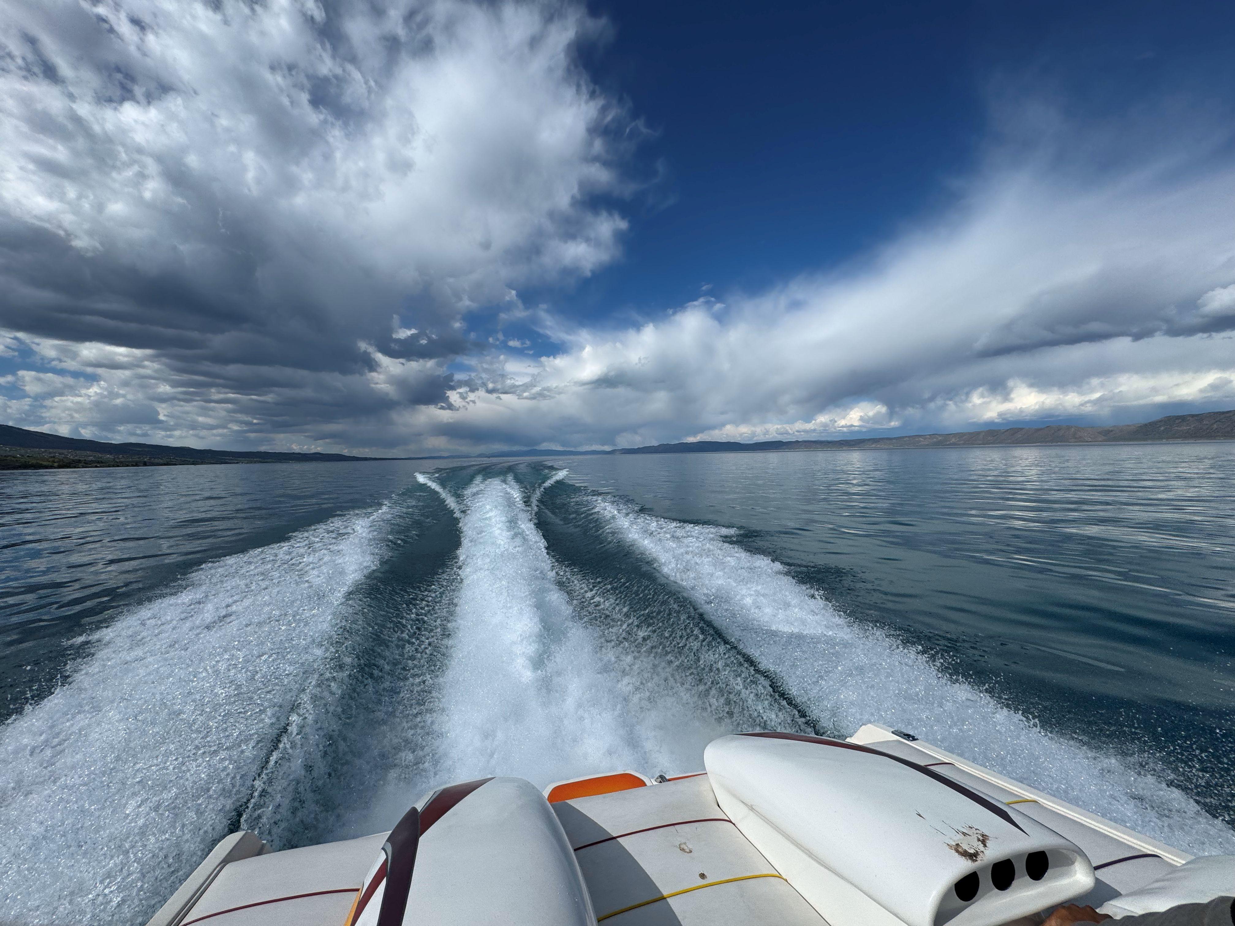 Speedboat cruising on a lake, leaving a wake under dramatic cloudy skies.