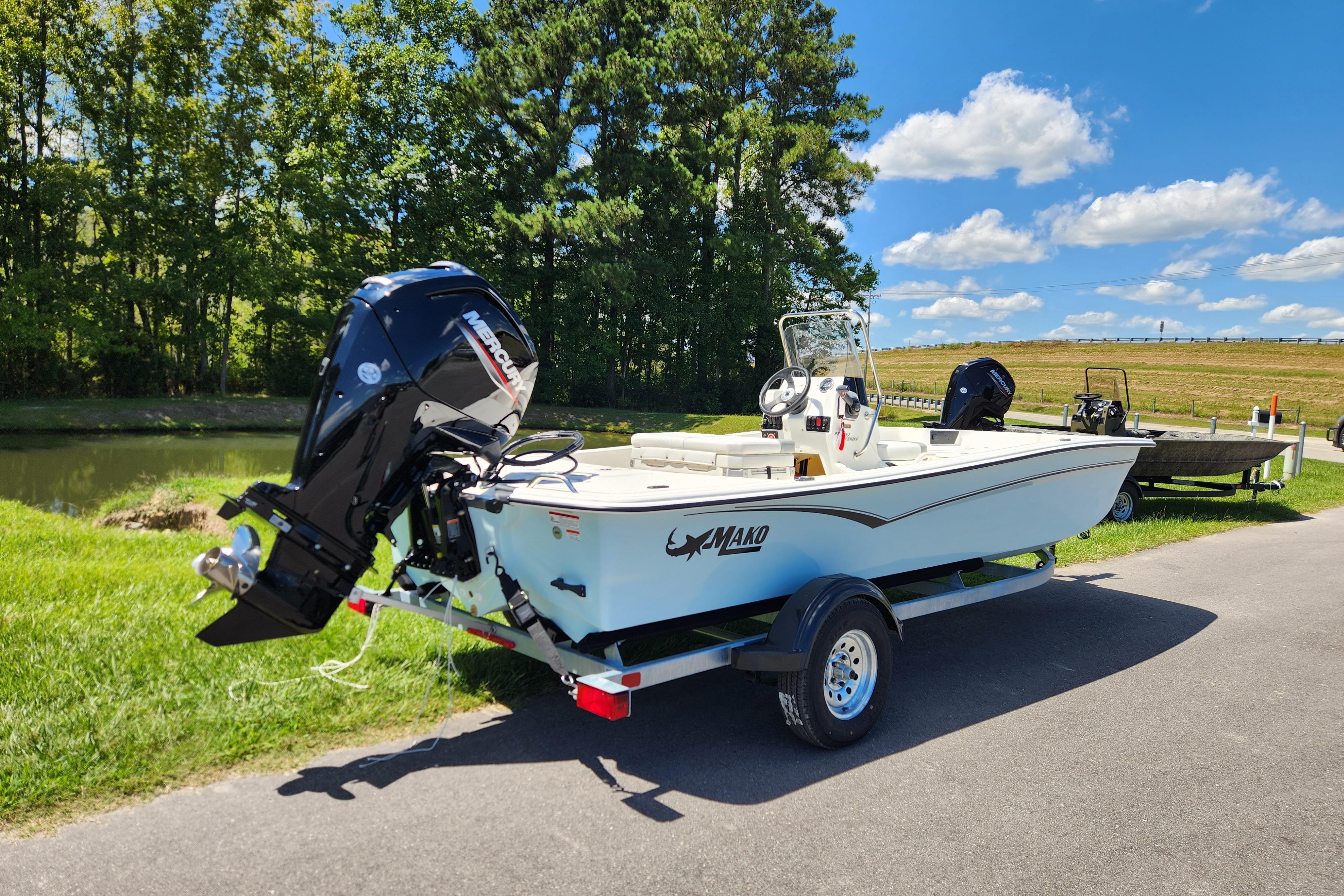 2026 Mako Pro Skiff 17 CC boat on trailer, parked near a pond under blue sky.