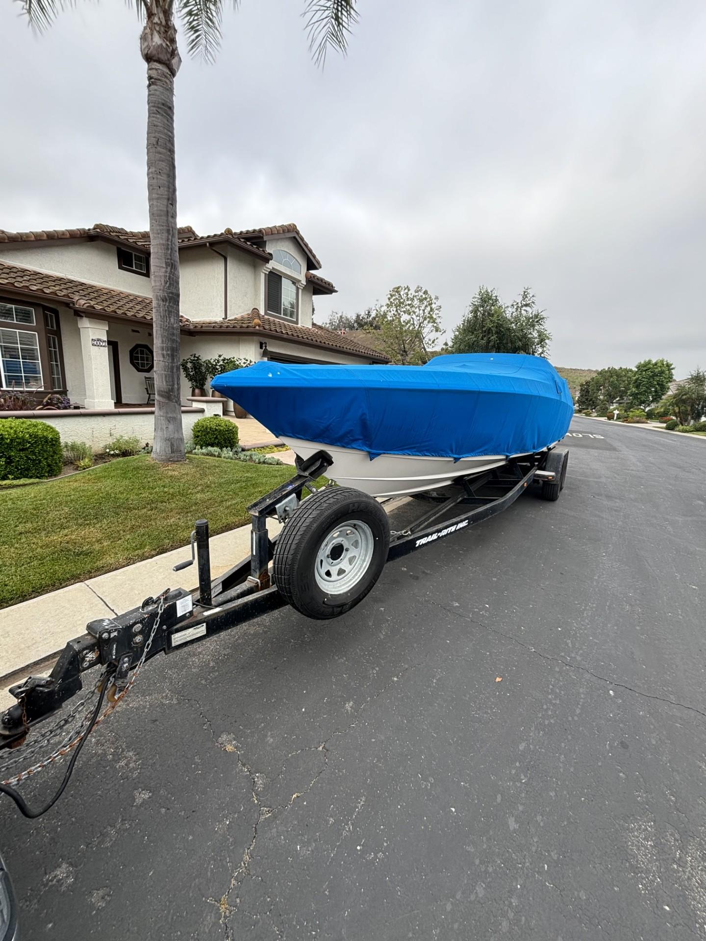 1998 Wellcraft Scarab 30 boat on trailer with blue cover, parked on residential street.
