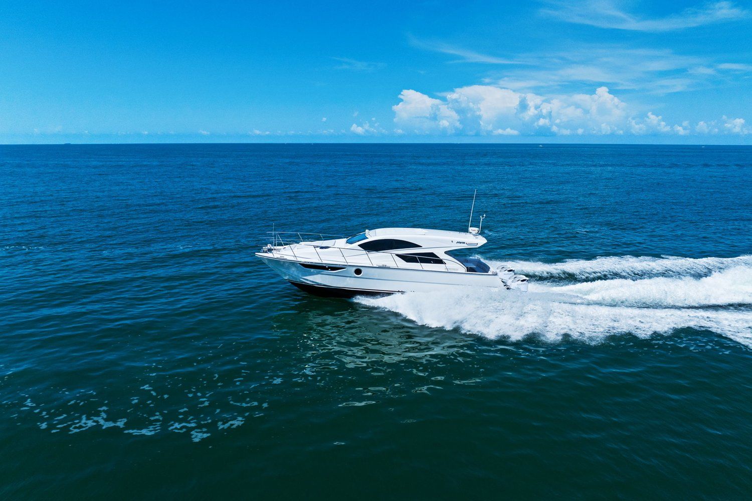 A white catamaran speeds across the blue sea under a clear sky.