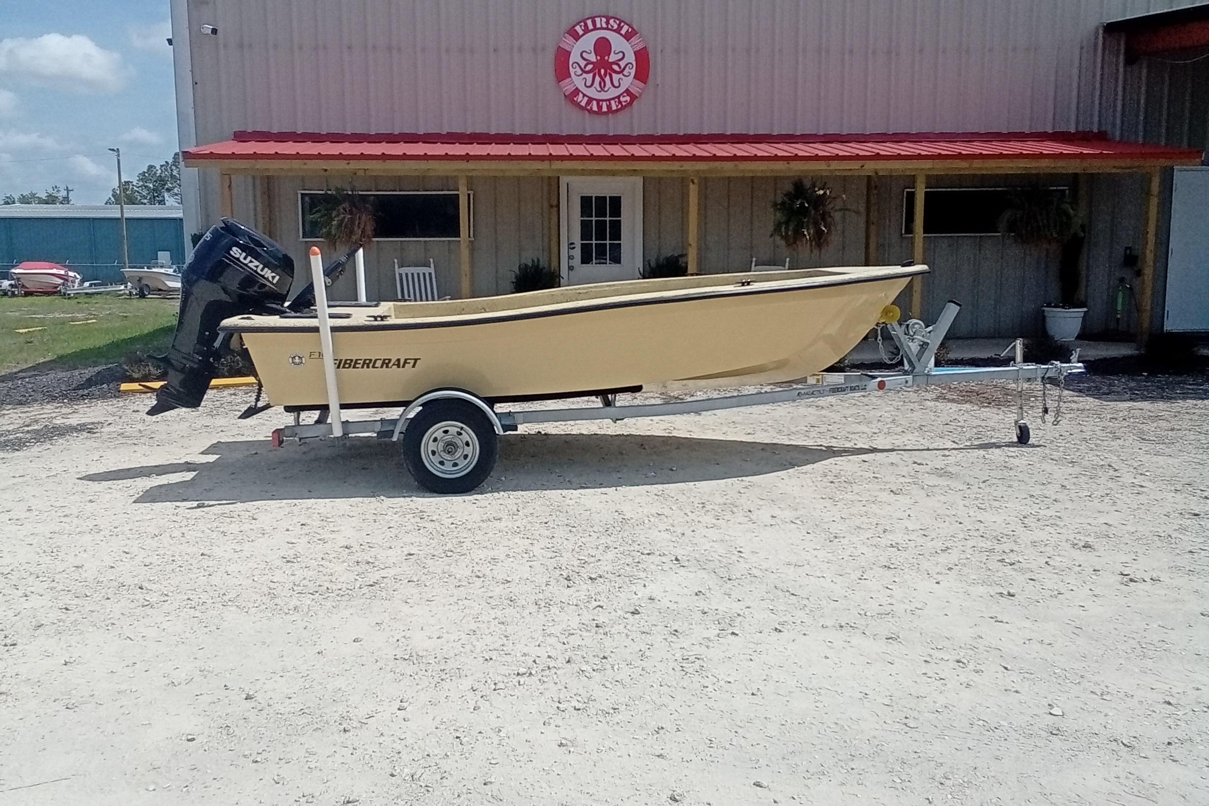 2025 Fibercraft F16 boat on trailer with Suzuki outboard motor, parked outside a building.