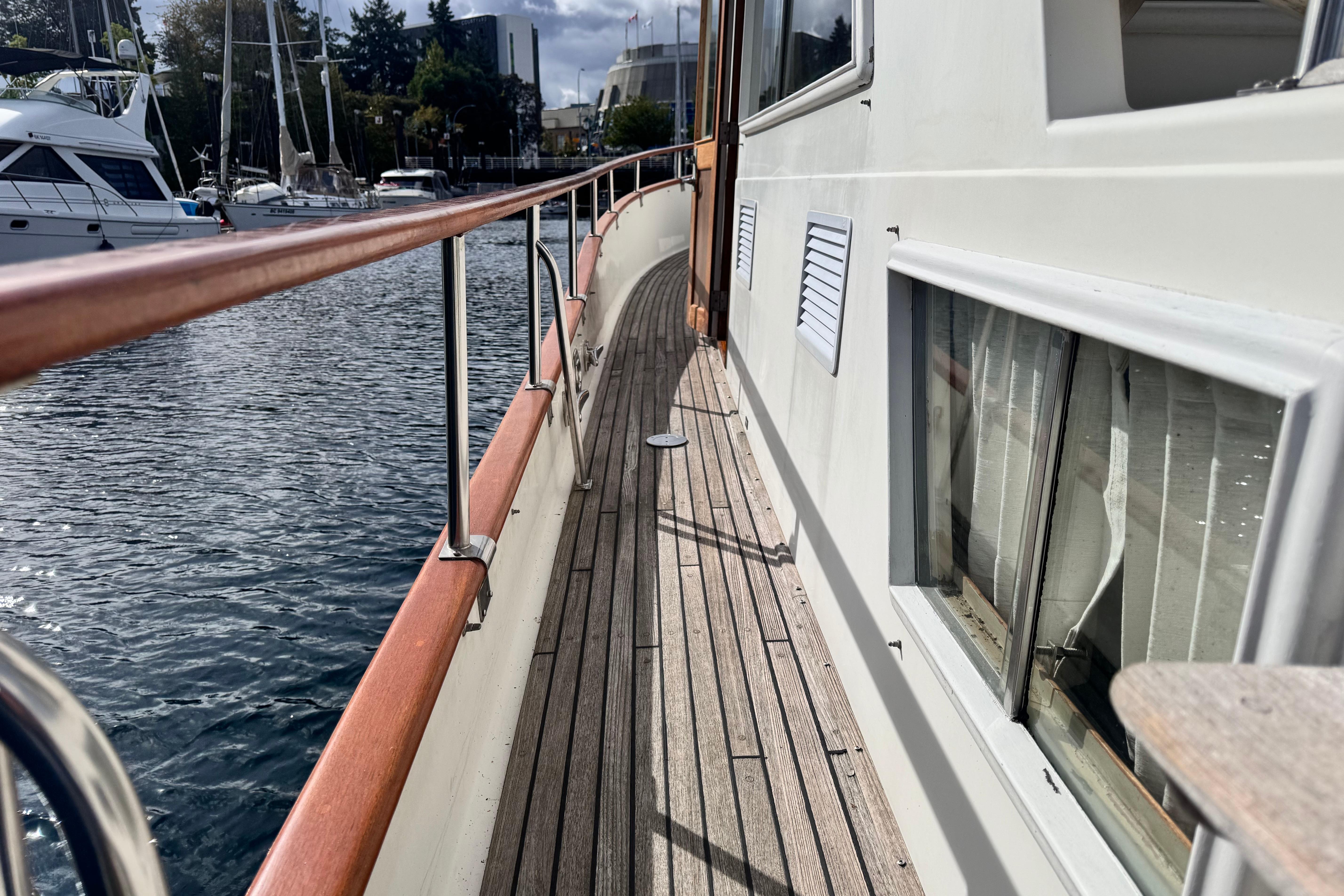 Side deck view of 1989 Grand Banks 42 yacht, featuring wooden railings and marina backdrop.