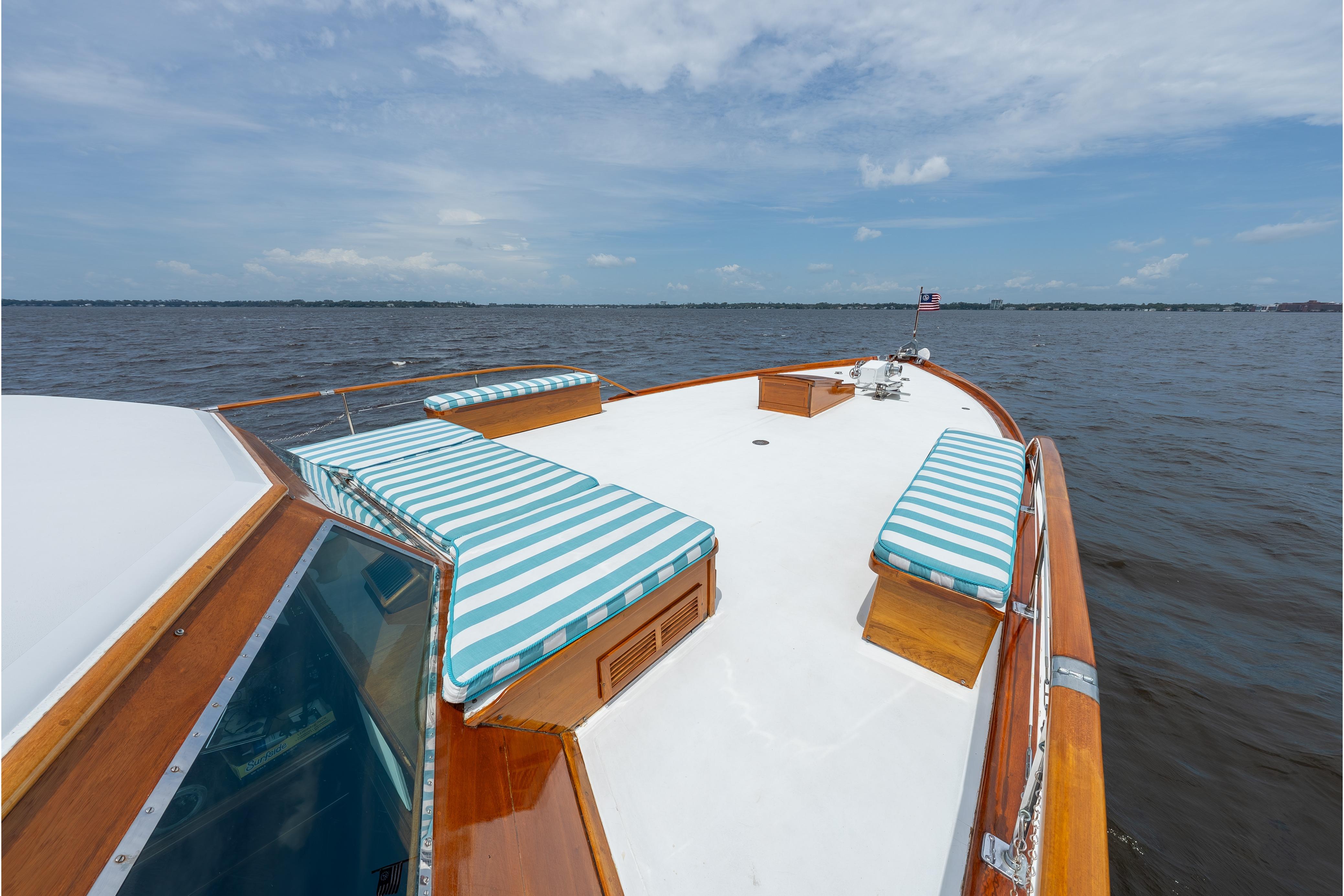 1963 Trumpy Classic yacht deck with striped cushions, cruising on open water under a blue sky.