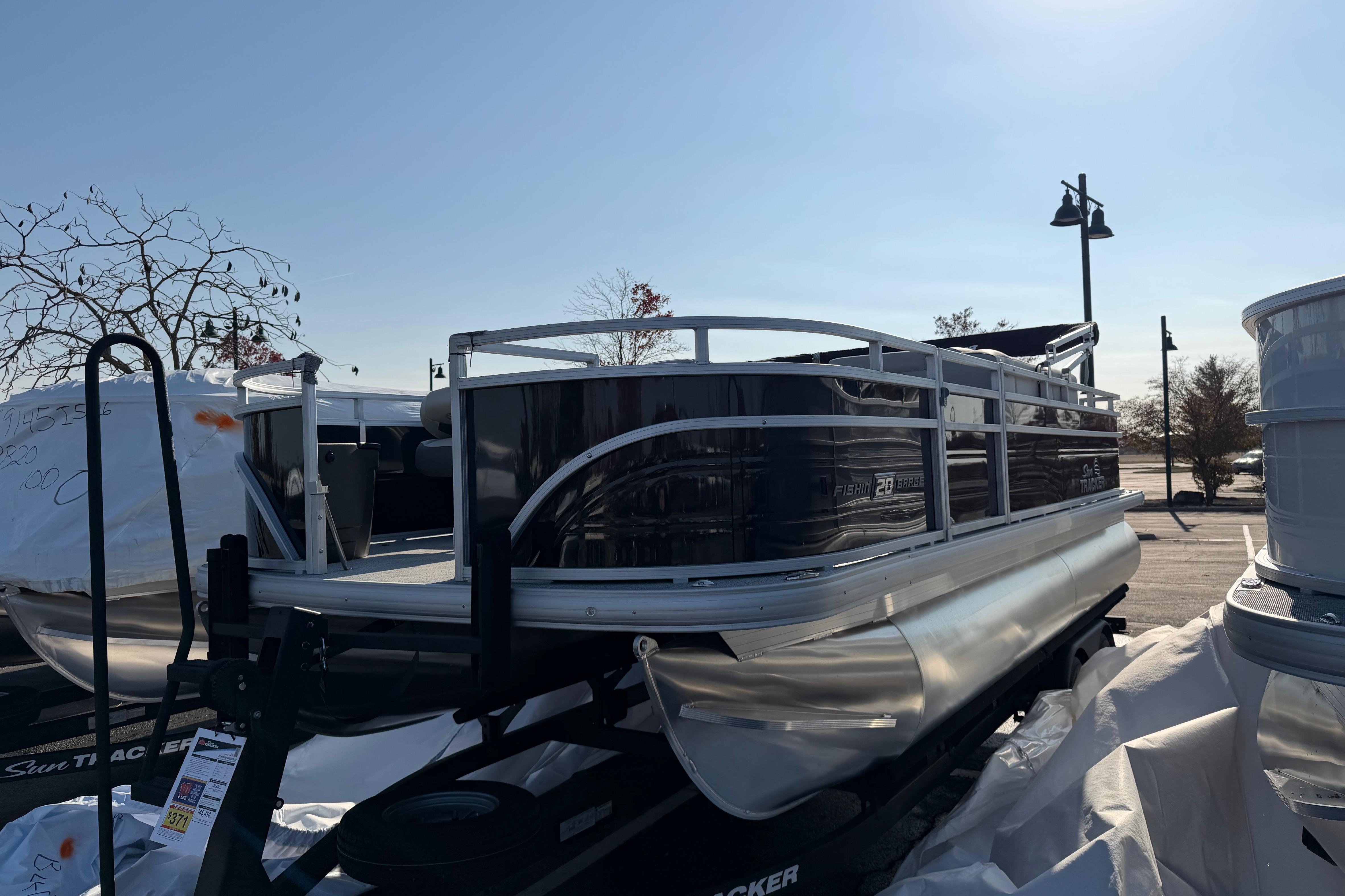 2026 Sun Tracker Fishin' Barge 20 DLX pontoon boat on trailer in parking lot.